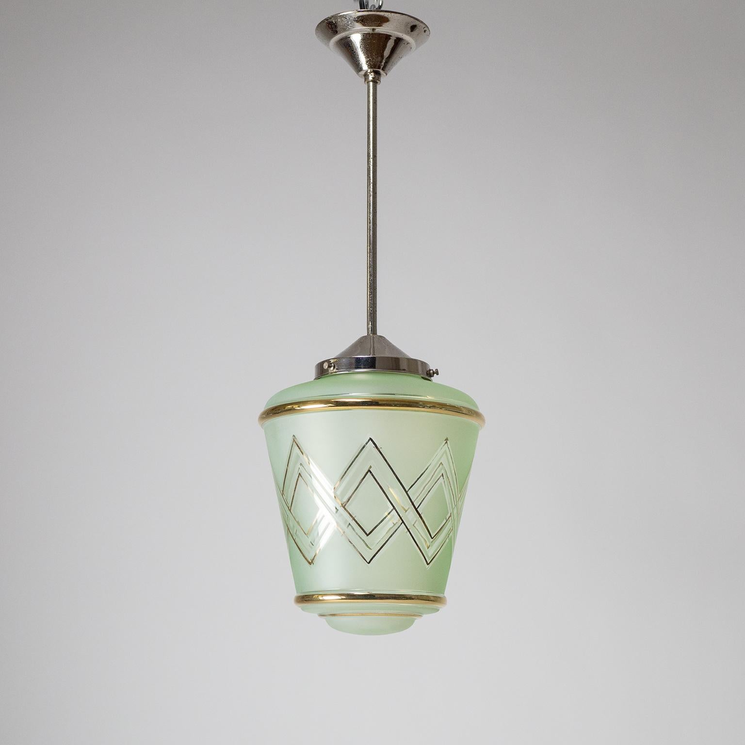 Lovely pair of French Art Deco pendants from the 1940s. Suspended from nickeled brass hardware are lantern-shaped blown glass diffusers with a mint green tint. The glass bodies are frosted on the outside with clear areas and gold paint in a