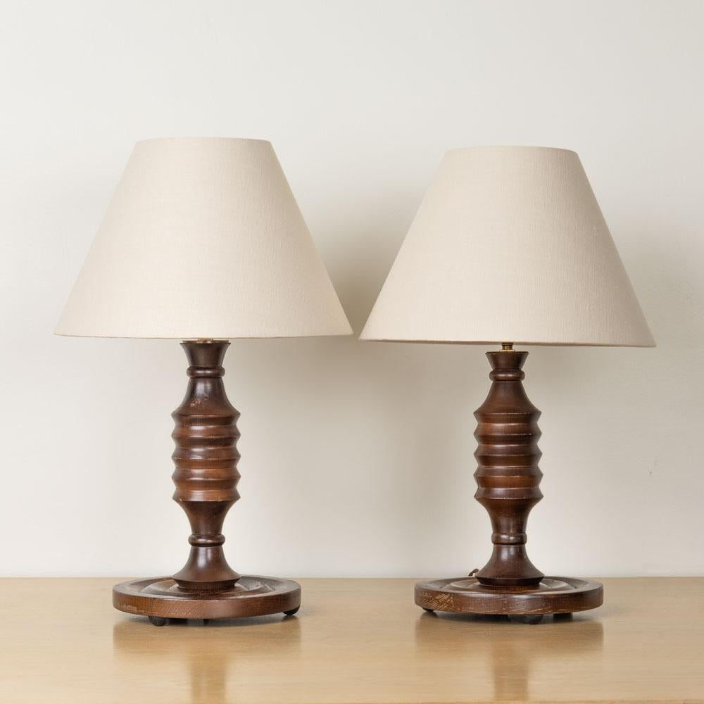 Great pair of carved wood table lamps from France, 1940s. Beautiful carved stem on circular base with three ball feet. Newly rewired and new linen shades. Original wood finish shows nice age and patina. One lamp is 1/4