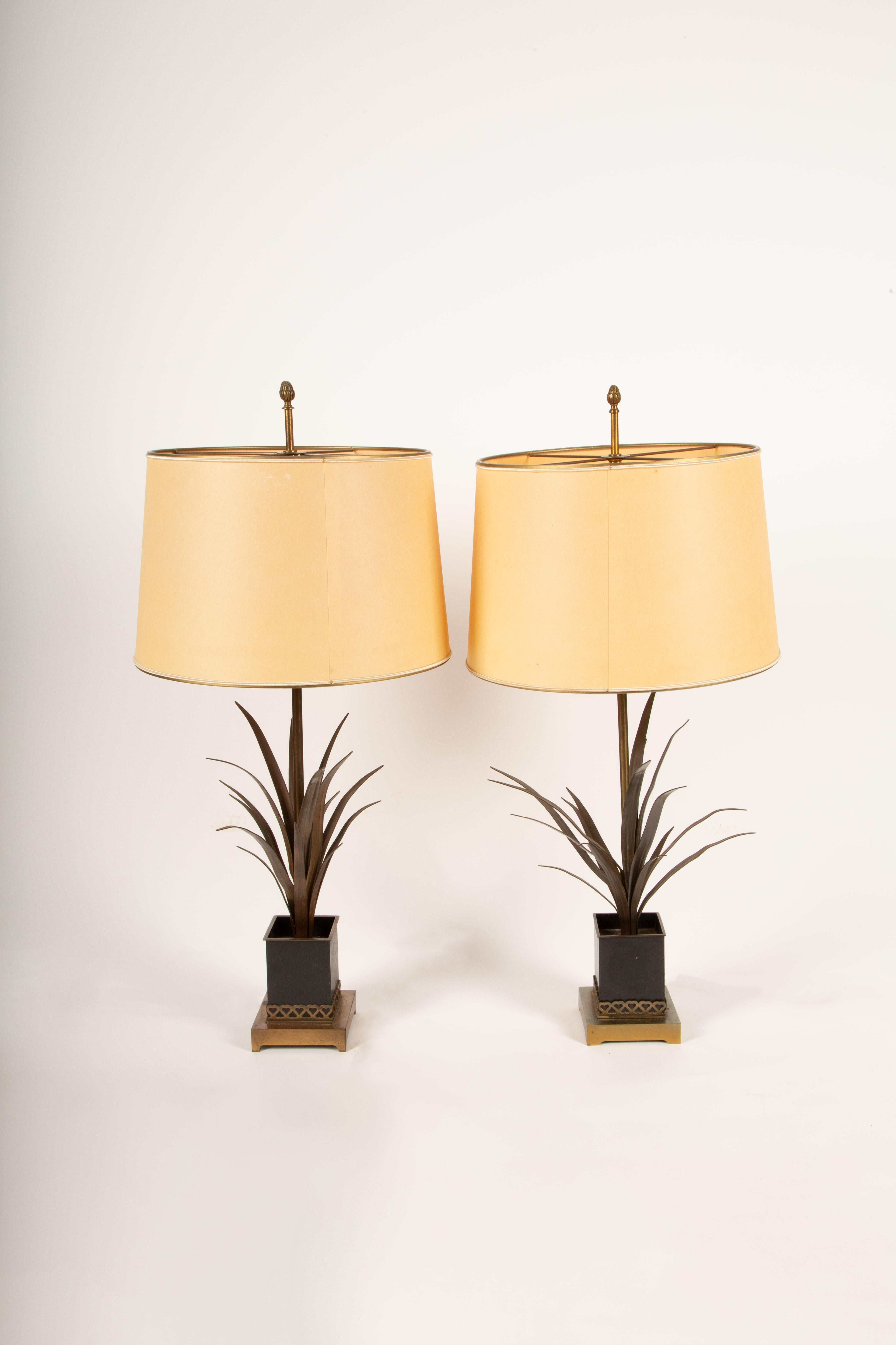 A sophisticated pair of 1940s French patinated bronze table lamps, intricately detailed to resemble stylized wheat or palm fronds rising from elegant cache pots. The bronze bases showcase exceptional craftsmanship, with a rich patina that enhances