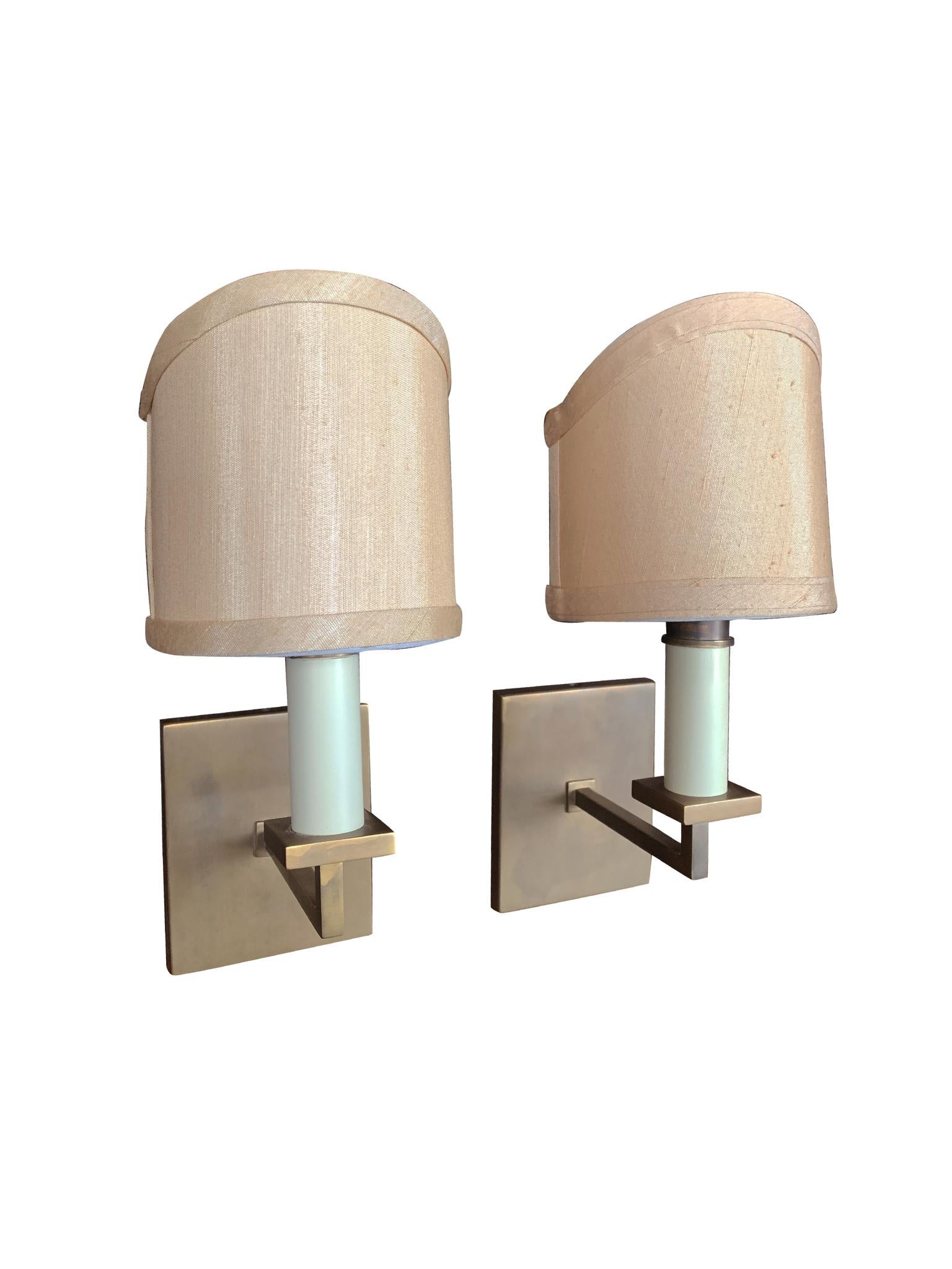 A classic pair of wall sconces made in France in the 1940s. They are brass with candelabra-style sockets. The custom shades are new. They have an elegant shield structure and are comprised of a pale-peach silk with a resin backing. These sconces are