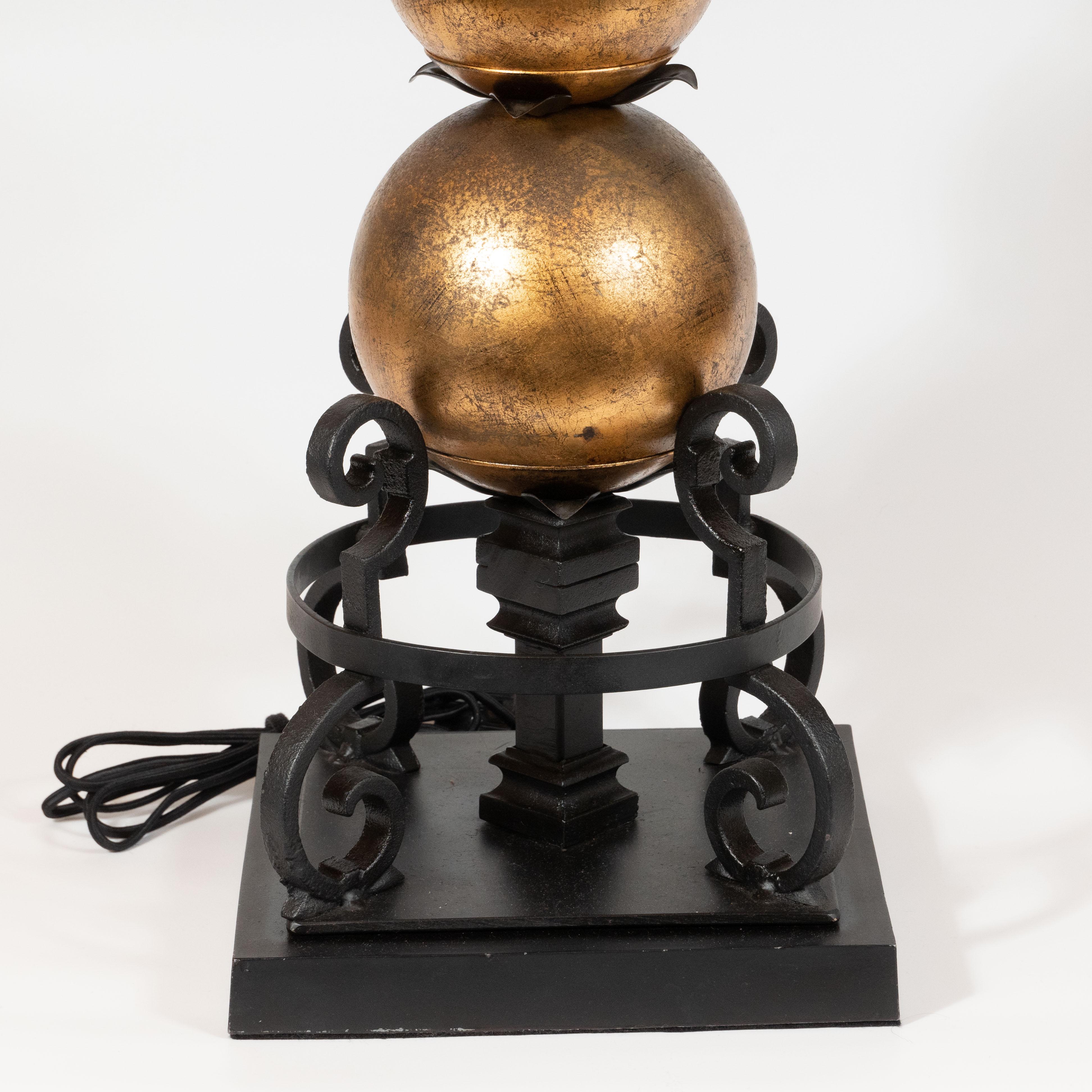 This dramatic and architectural pair of table lamps were realized in France, circa 1940. They feature Edgar Brandt style wrought iron curvilinear embellishments ascending from a square skyscraper style base of the same material. Spherical gilded