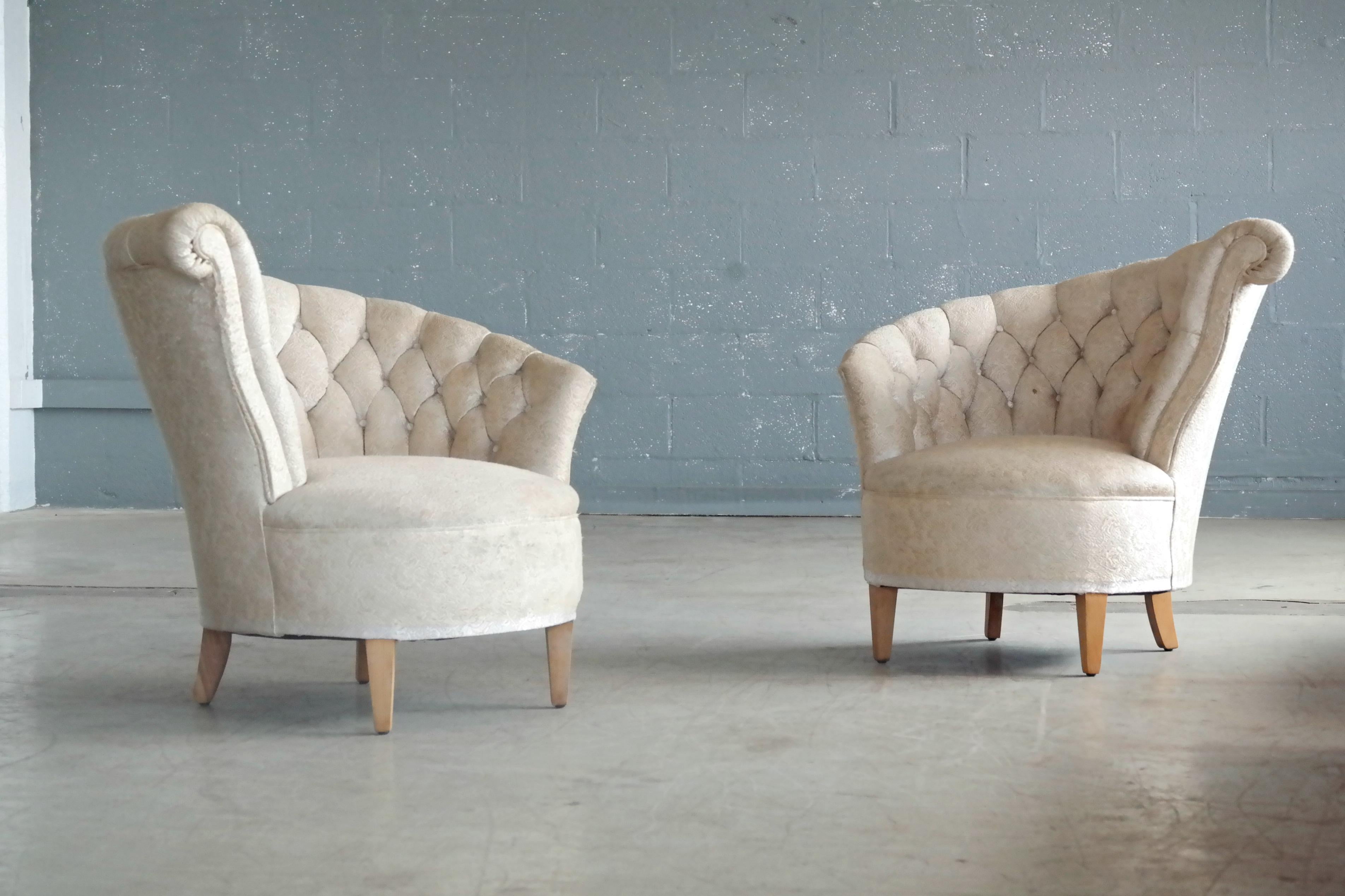 Whimsical and glamorous pair of 1940s Hollywood Regency style lounge chairs. The chairs have a circular design when seen from above and the backs of each chair feature an asymmetrical fan back design with tufted upholstery and a slight scroll detail