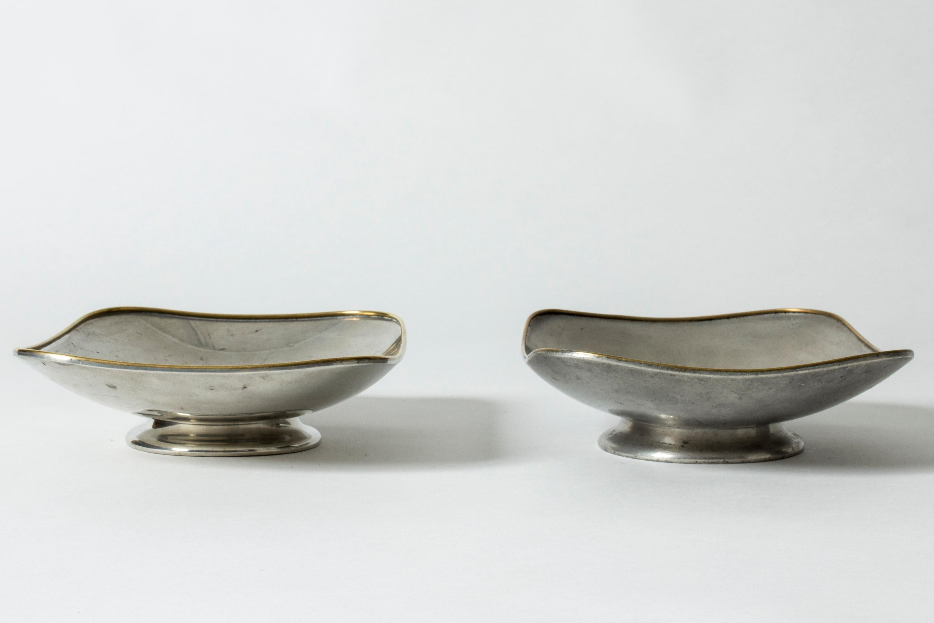 Pair of pewter serving platters by Nils Fougstedt, in a crisp modernist design. Clean lines with rounded corners, rims framed with brass lines. One is more matte while the other has a more polished finish.