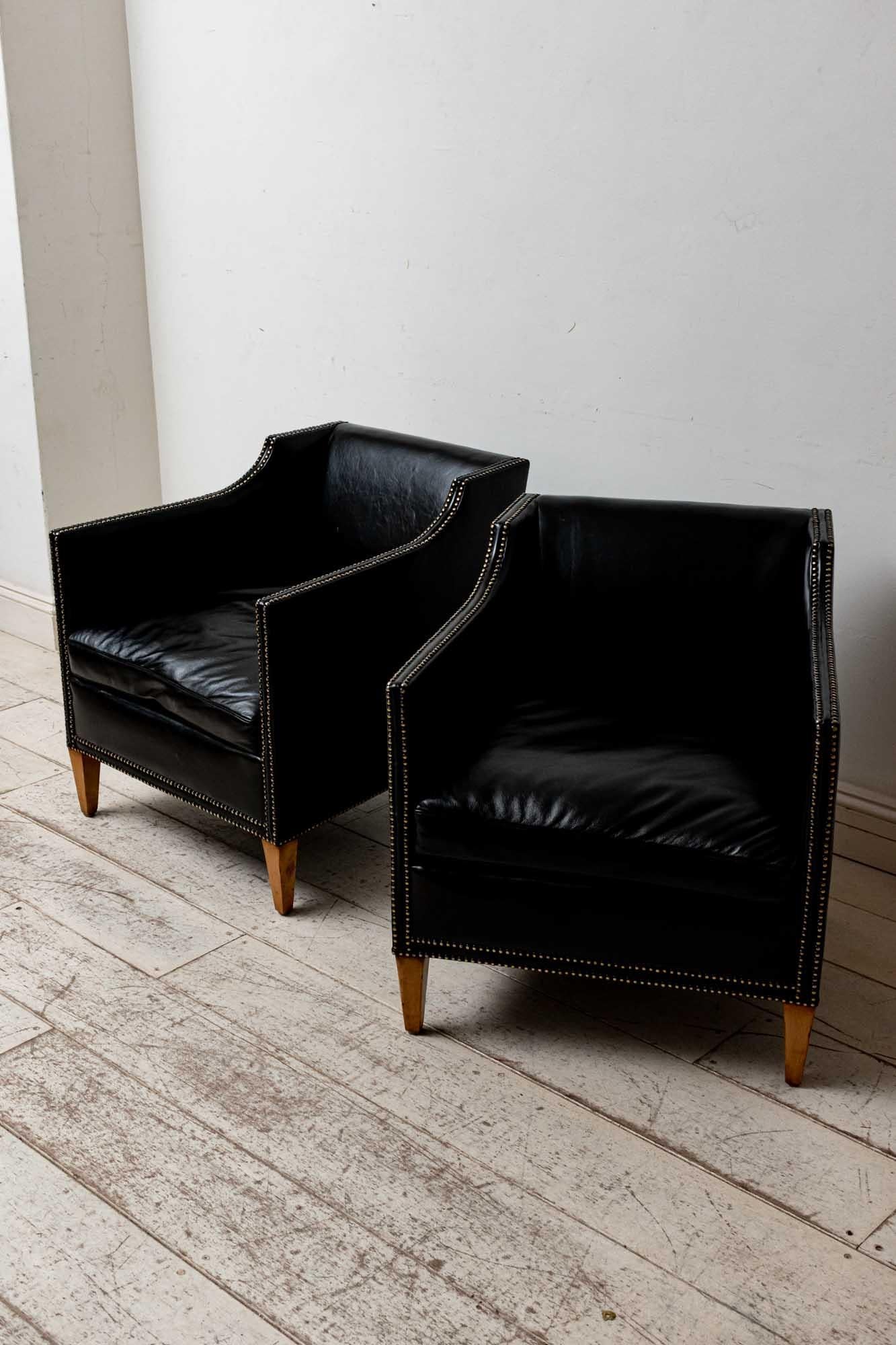 A fabulous pair of very smart Swedish armchairs which have been newly reupholstered in black leather with a double row of brass studded detailing to the arms and square tapering feature wooden legs. 
The armchairs have feather filled seat cushions