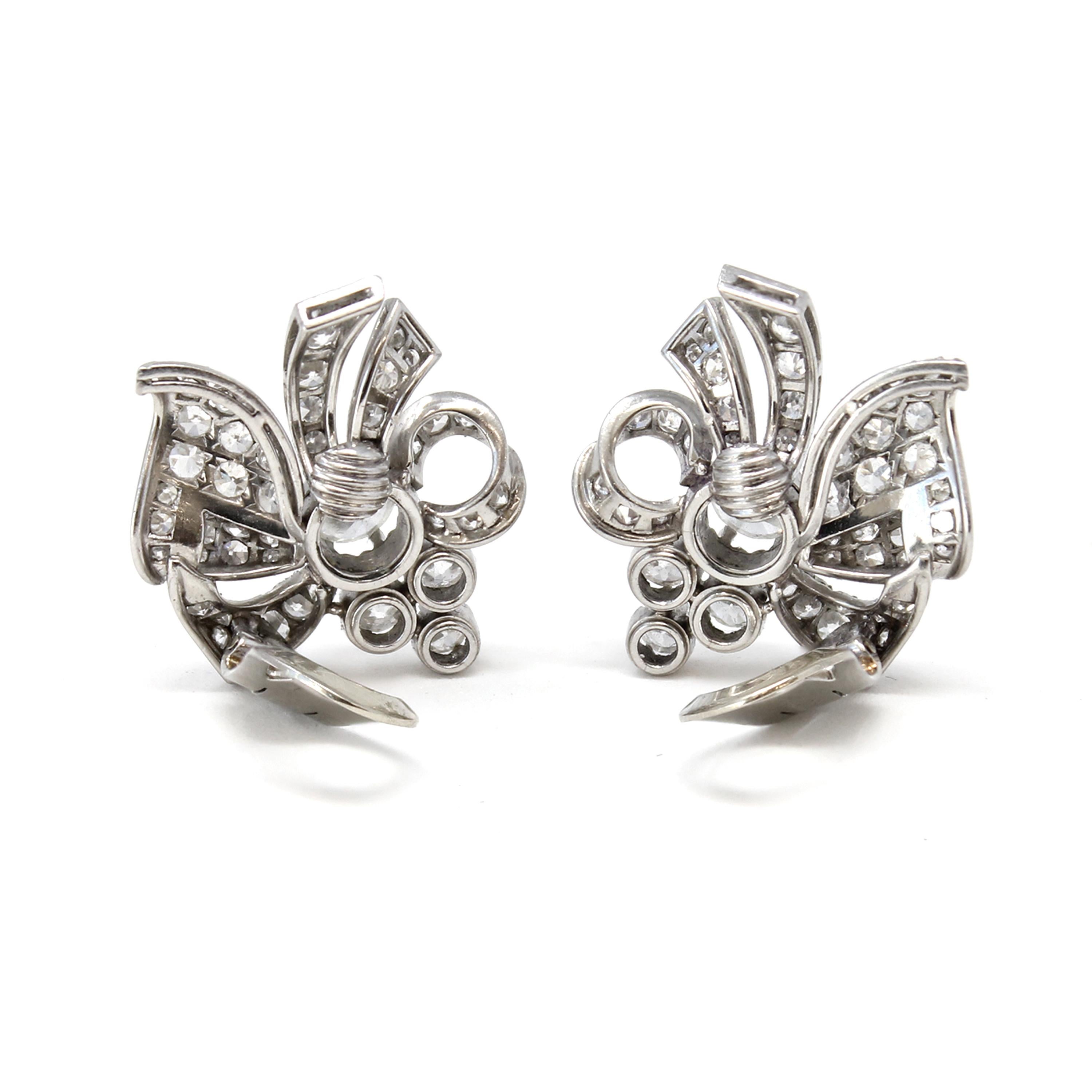 A pair of vintage mid-century Platinum and Diamond clip bow-style earrings from the late 1940s. Delicate volutes accented with sparkling Diamonds surround in a graceful movement the 3.50 carat Diamond that adorns the center of each earring.