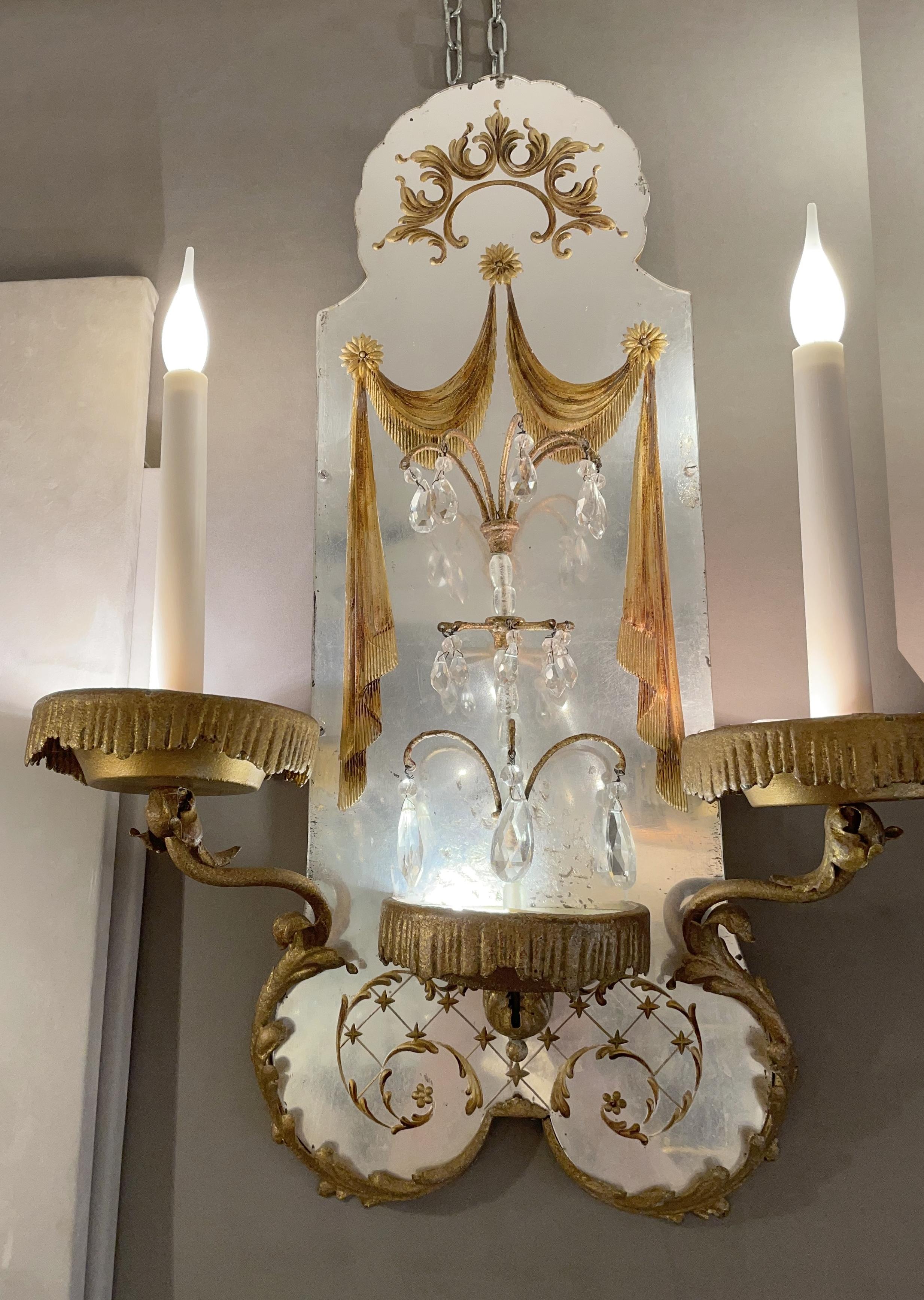 Two wall lights in the style of Maison Baguès made with gilded iron, églomisé plexiglass, and crystal pendants.
For each sconce, the seven lights are located on the two candles and the three bobeches, at the base of each candle and in the central
