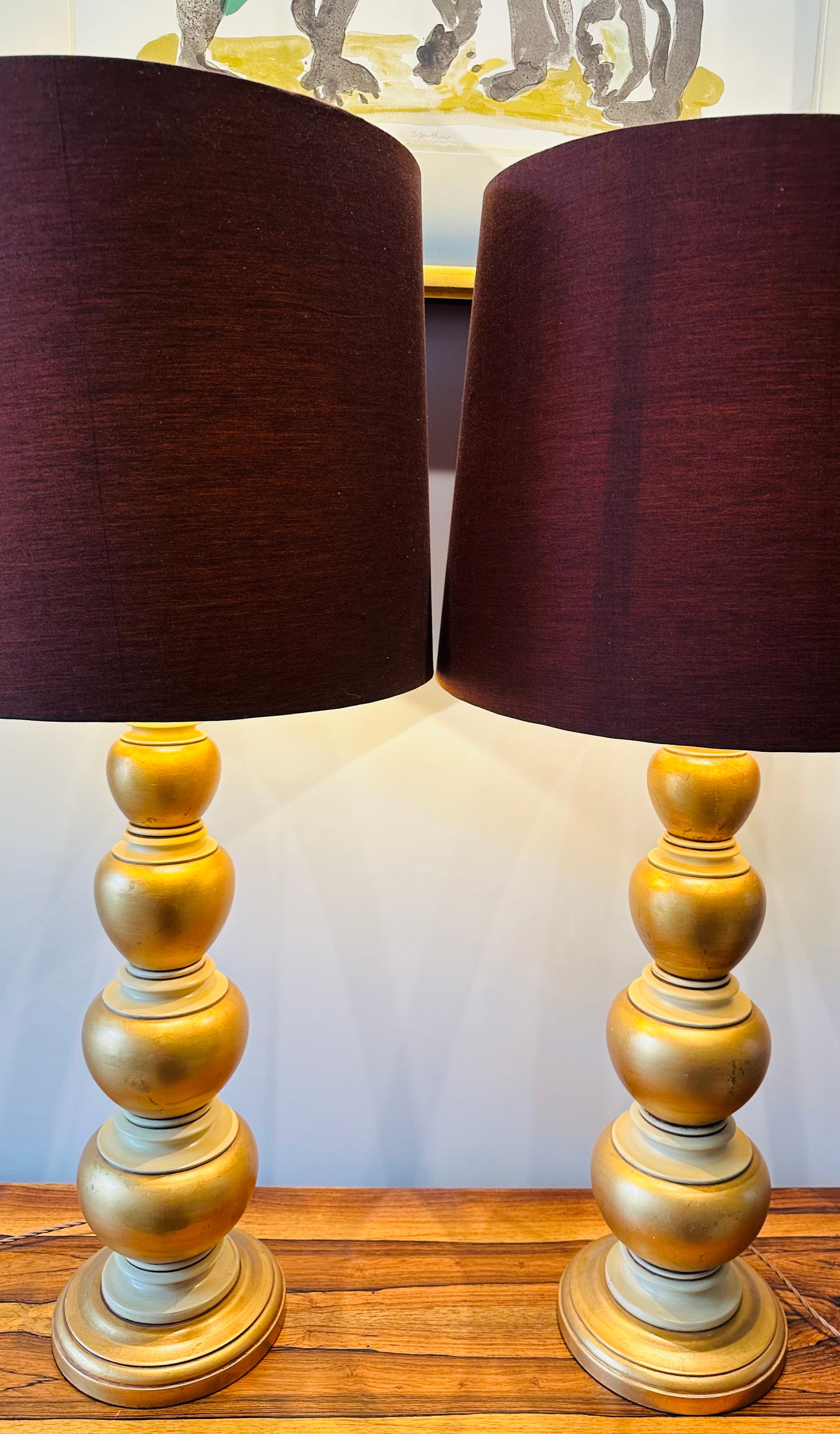 Pair of 1950s American Frederick Cooper tall gold leaf and cream painted table lamps which are often mistaken and are in the style of James Mont. The lamps are constructed from heavy turned wood which have been carved to form four concentric oval