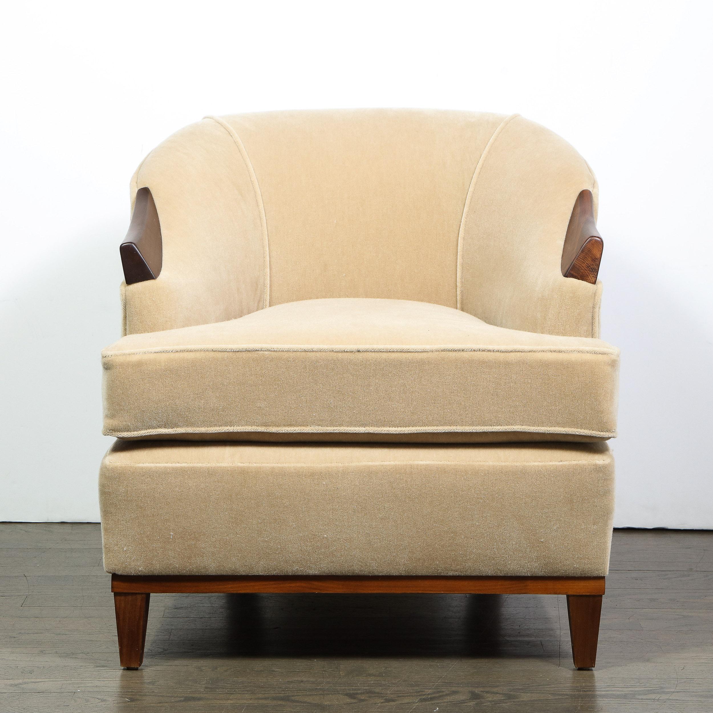 This stunning pair of Mid-Century Modern club chairs were realized in the United States, circa 1950. They featured tapered volumetric rectangular front legs, and stylized saber hind legs in hand rubbed walnut- a material that recurs on the