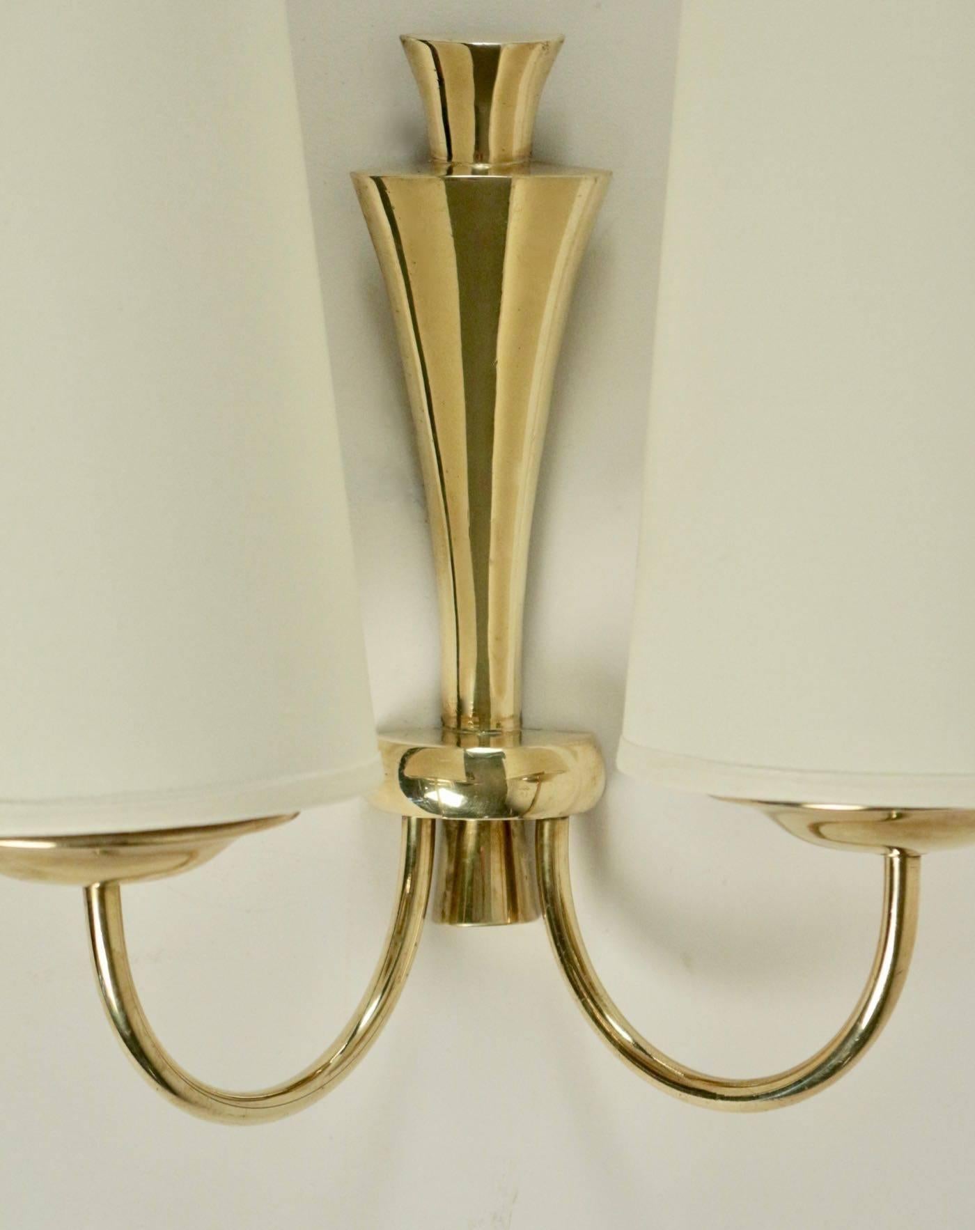 Pair of 1950s Arlus brass sconces.

Two curved arms with cup, and back plate made of gilded brass.
Handmade lampshades of white cotton granted to the originals.

Two bulbs per sconces.
 