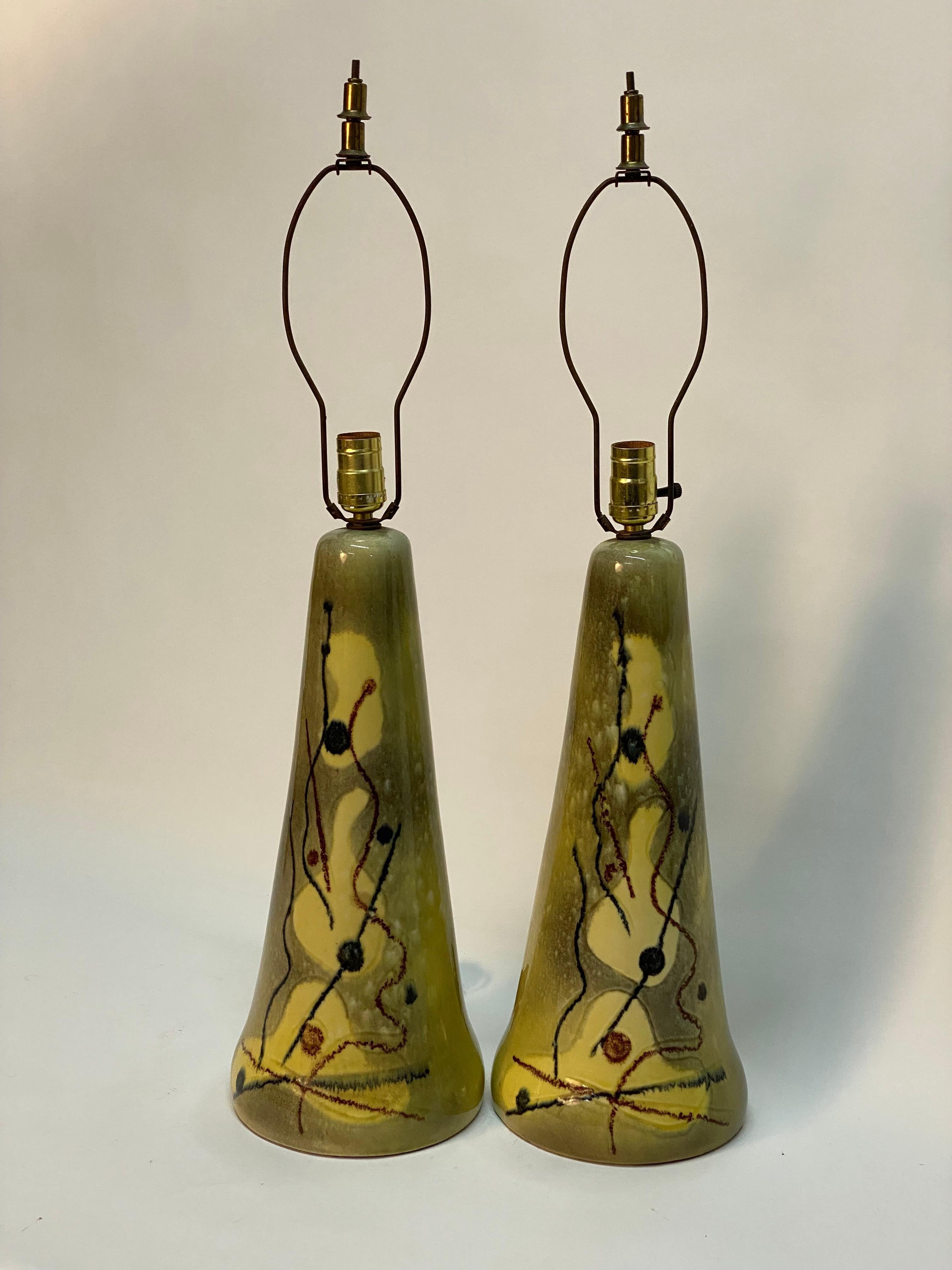 A smart looking pair of abstract decorated 1950s ceramic table lamps in the manner of Yasha Heifetz or Marianna Von Allesch. High gloss chartreuse glaze with a biomorphic abstract motif on a tapered cone shaped ceramic body. Original working wiring.