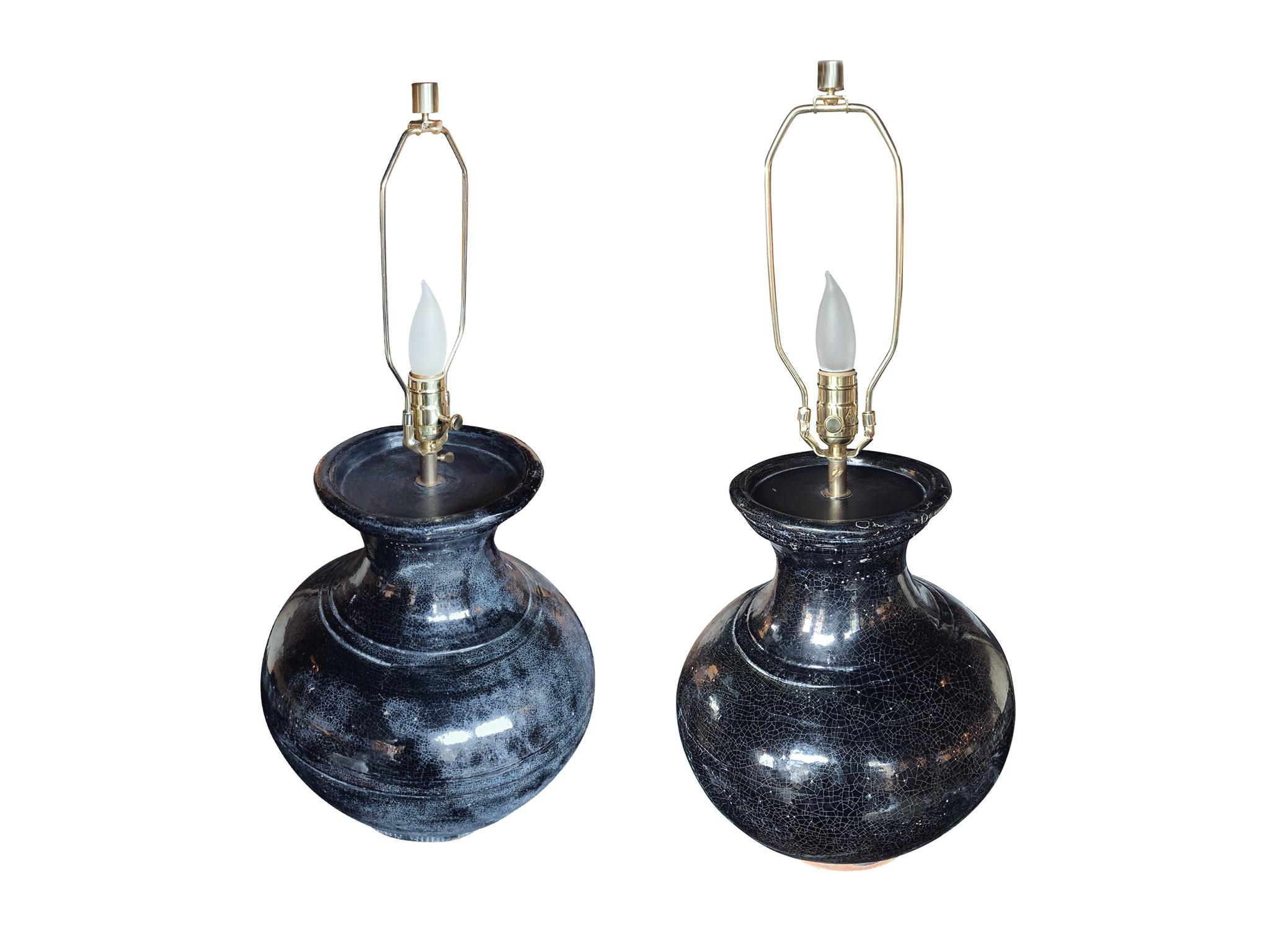 An exquisite pair of midcentury vase lamps. They are comprised of ceramic bodies with a near-metallic black glaze and craquelure textures. The lamps are newly rewired and refurbished with new brass hardware, which includes the finials, harps, and