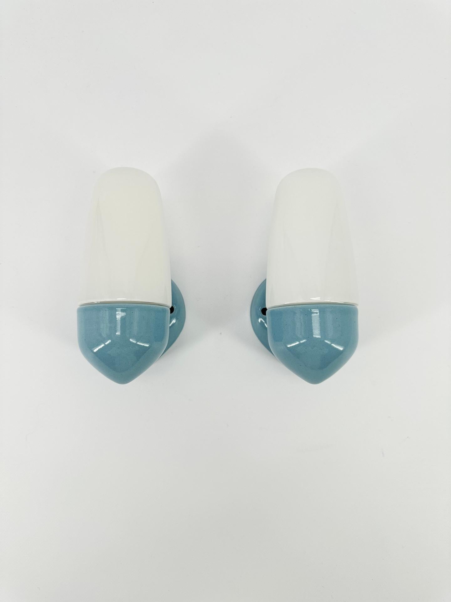 Paire d'appliques en porcelaine bleue et abat-jour en verre opalin conçues par le designer allemand Wilhelm Wagenfeld, qui a étudié à l'école du Bauhaus. 

Datant de 1958, cette applique murale présente des lignes épurées, rondes et élégantes, un