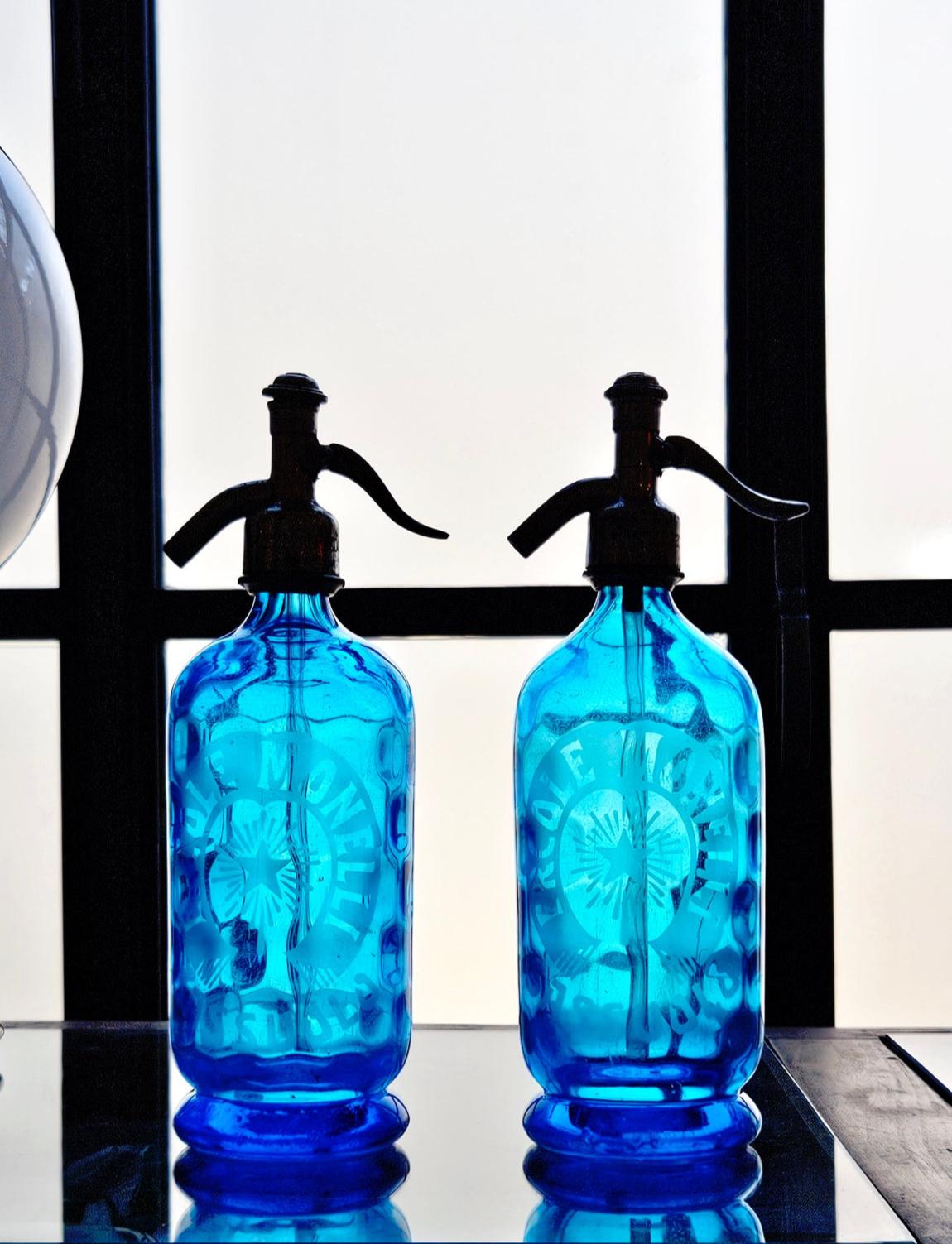 A pair of 1950s Blue Soda Bottles etched with the name of the owner and the town, Ercole Monelli, Sassuolo. Both bottles have wonderful decorative indentations in the glass. Spectacular decorative pieces for a home bar and display.