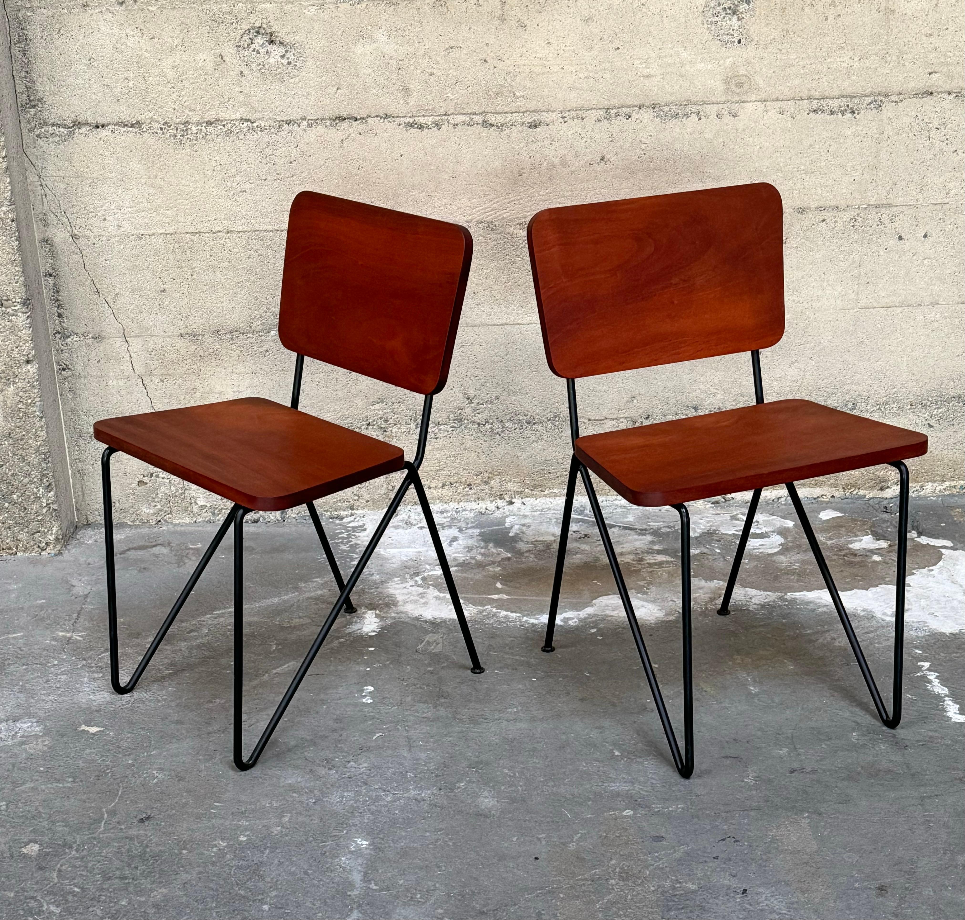 Pair of iron and tropical hardwood side chairs, hairpin wrought iron frames with wooden seats and backs in a rounded tapered triangle form. The wood is a rich red-brown with a slight black grain. The welded iron frames have a hairpin front wrapping