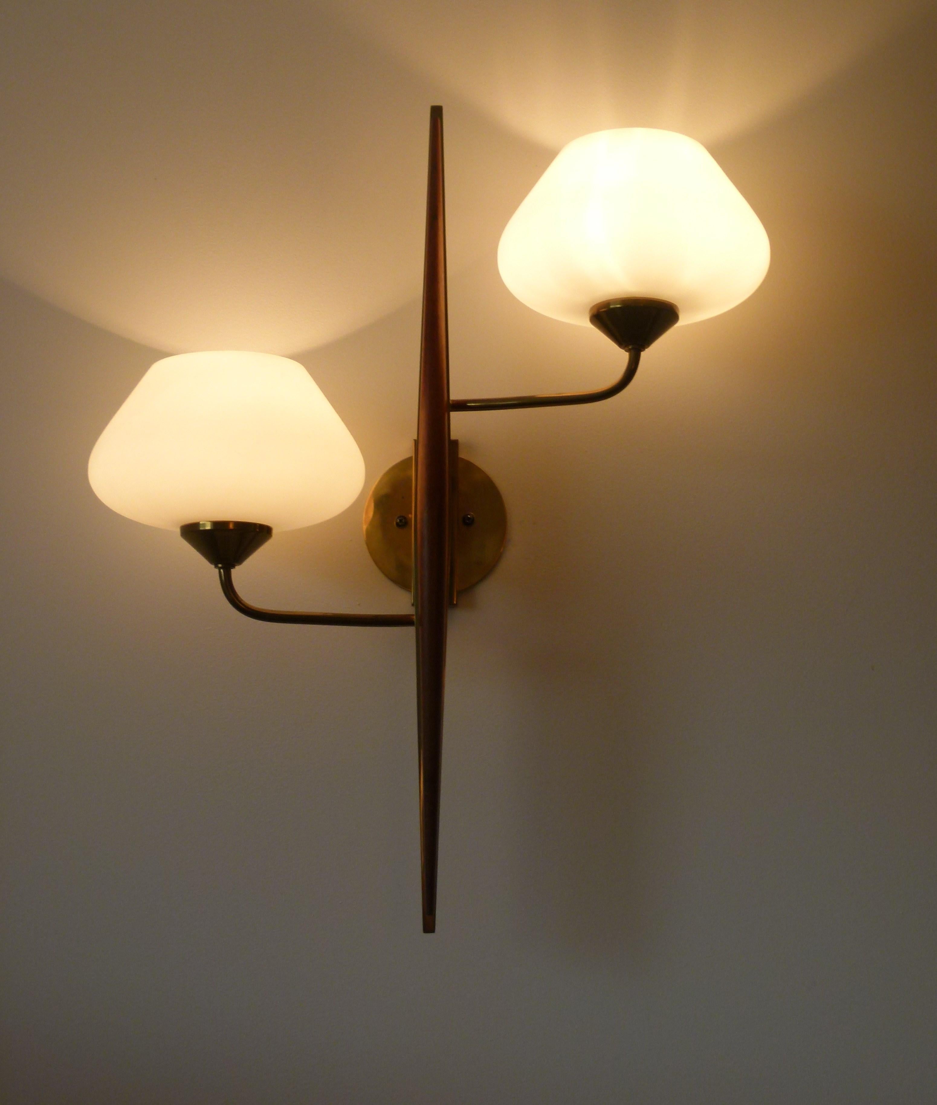 Pair of double wall sconces, consisting of a solid brass base, supported by two brass arms of light, surmounted by lampshades in frosted glass.
On the base is arranged a tapered varnished teak wood.
These sconces are in very good original