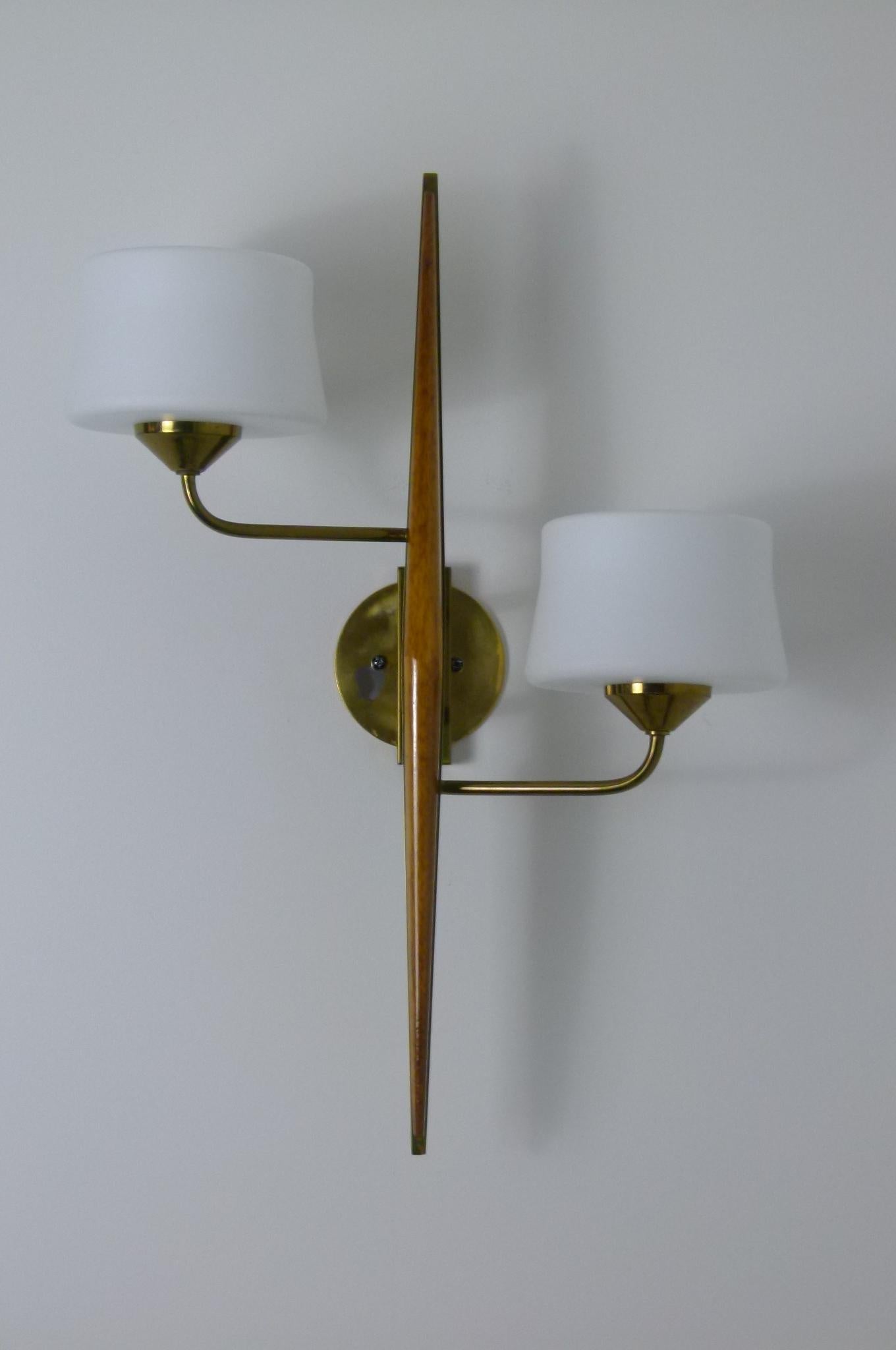 Pair of double-walled sconces, made of a solid brass base, supported by two brass sconces, topped with frosted glass shades.
On the base is laid out a tapered varnished teak wood.
The circular brass plate is not part of the sconces.
The support