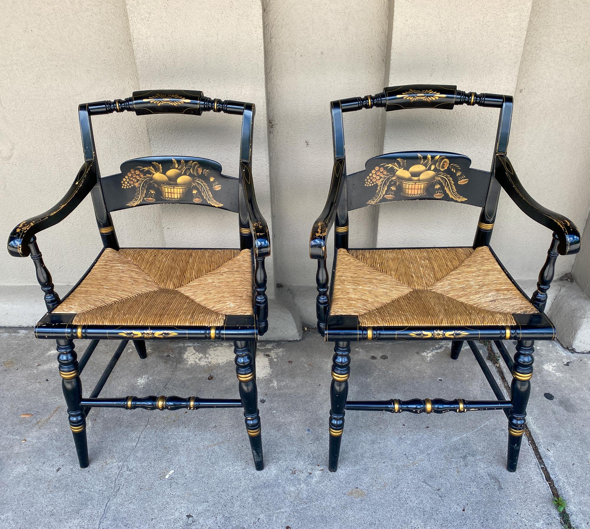 This pairing of armchairs is finished in a glossy black lacquer with gold details, with rush seats. The legs, arms and back rails all have turned details, with scroll-shaped armrests that have also been pinstriped in a gilt paint. The decoration is