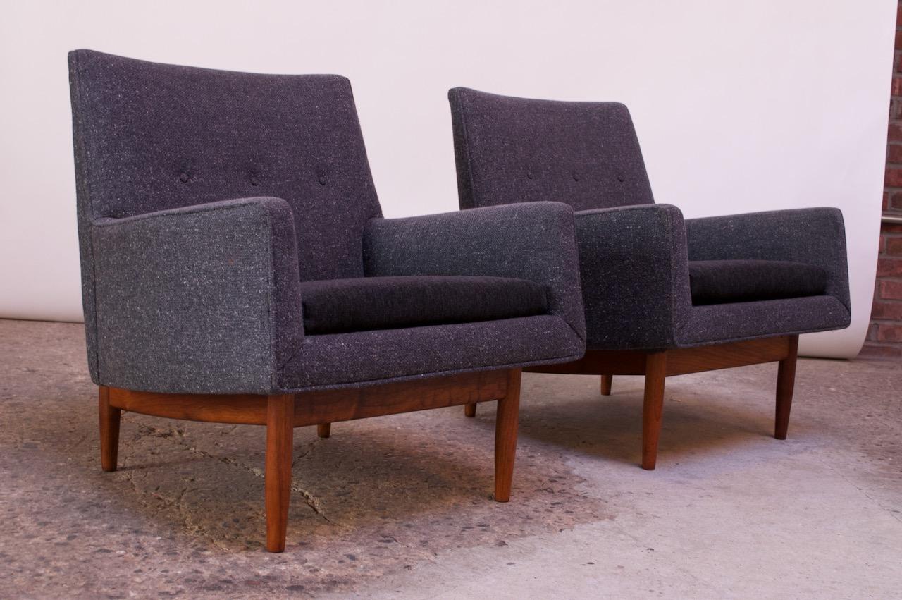 Jens Risom lounge chairs supported by walnut bases, circa 1953. They are relatively small in scale and boast clean, sharp lines. The frame's gray wool upholstery is original, featuring a back button-tufted detail. The cushions have been recovered in