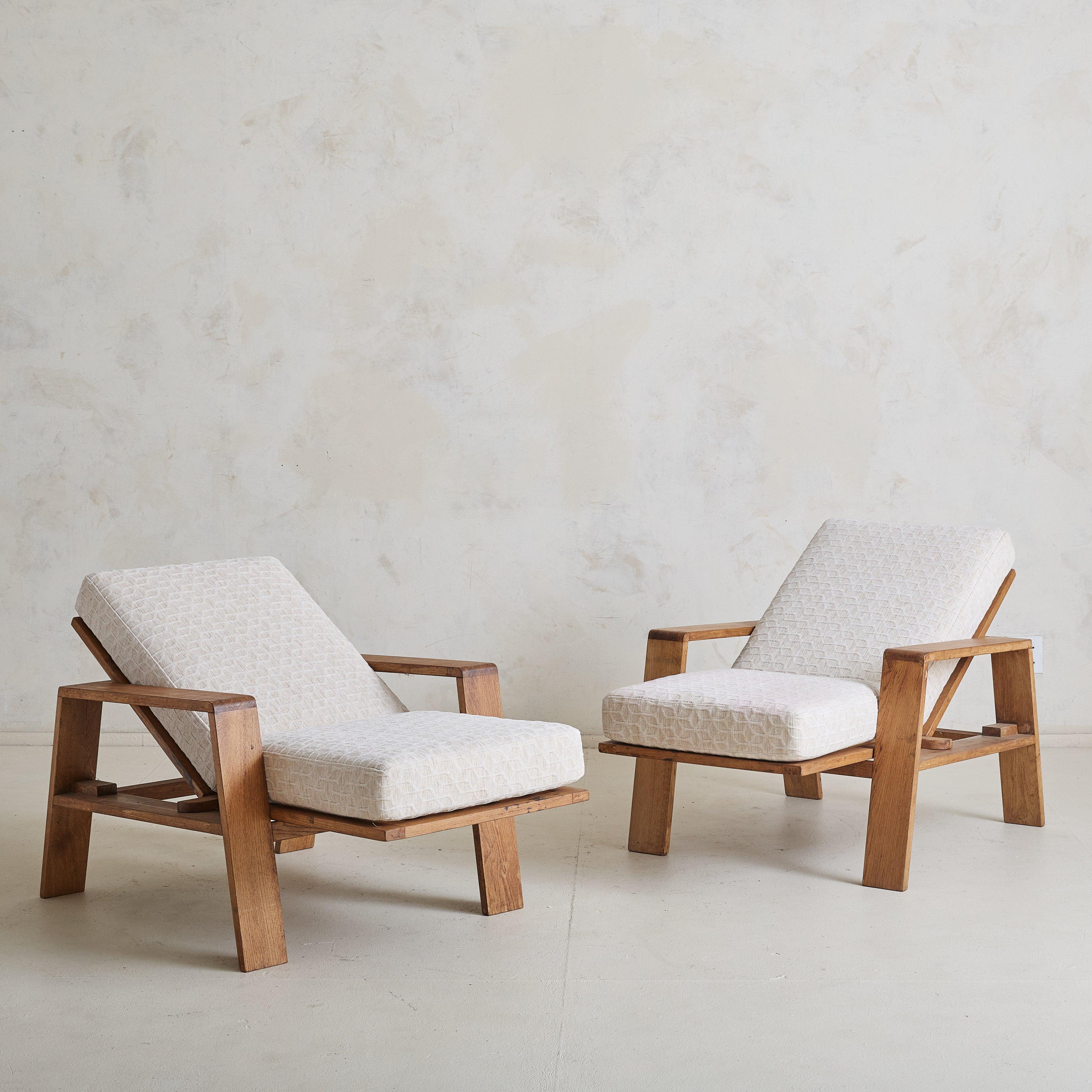 A pair of 1950s French reclinable oak armchairs. Constructed from solid oak, the frames feature slatted backs and angled legs, creating a relaxed, ergonomic silhouette. The chairs are adjustable—the seats cleverly slide forward, allowing the backs