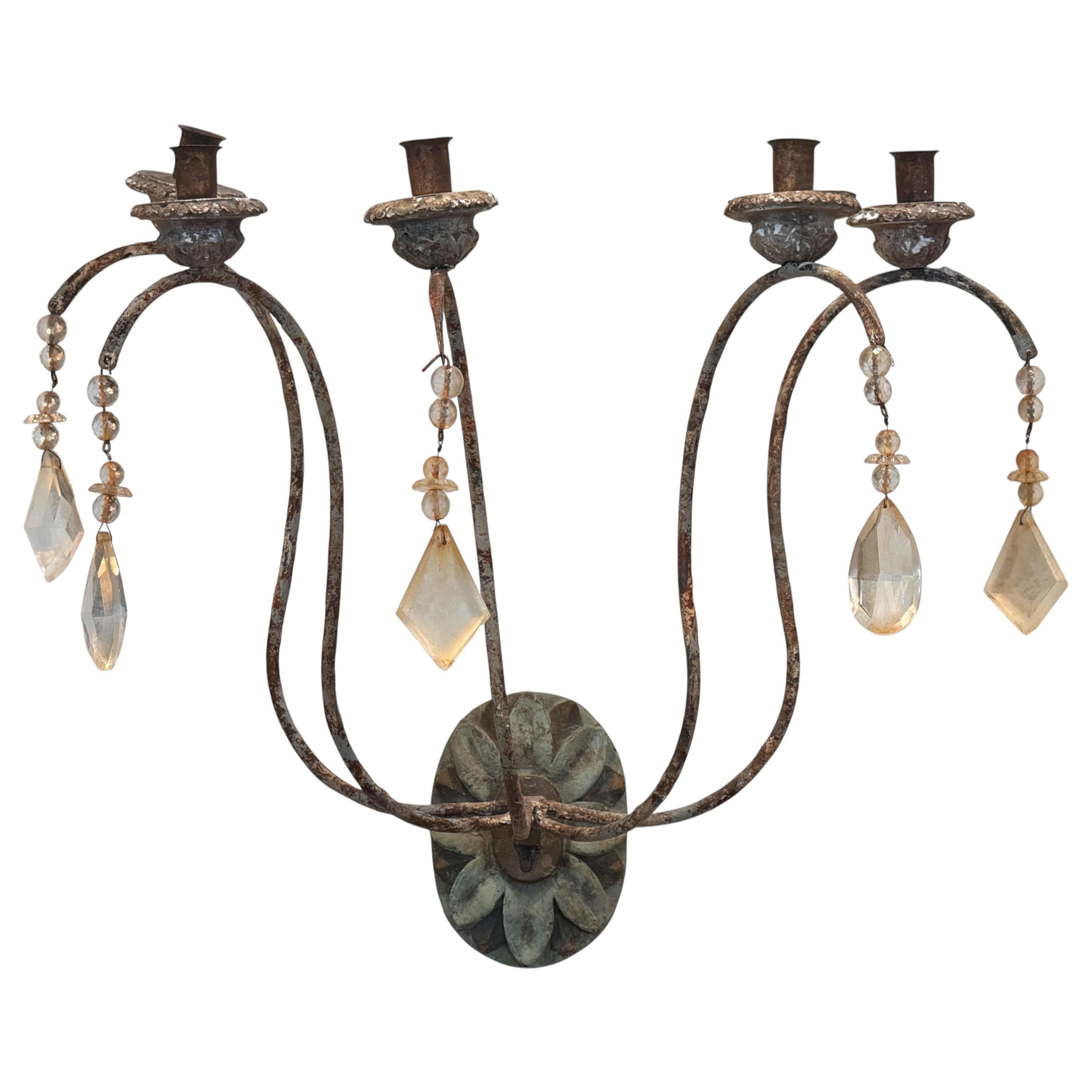 Pair of French Provincial-style wall sconces with scrolled iron arms and a rustic patina. Each sconce features three candle cups and is adorned with hanging glass prisms in varied shapes, adding a soft decorative accent to their understated form.