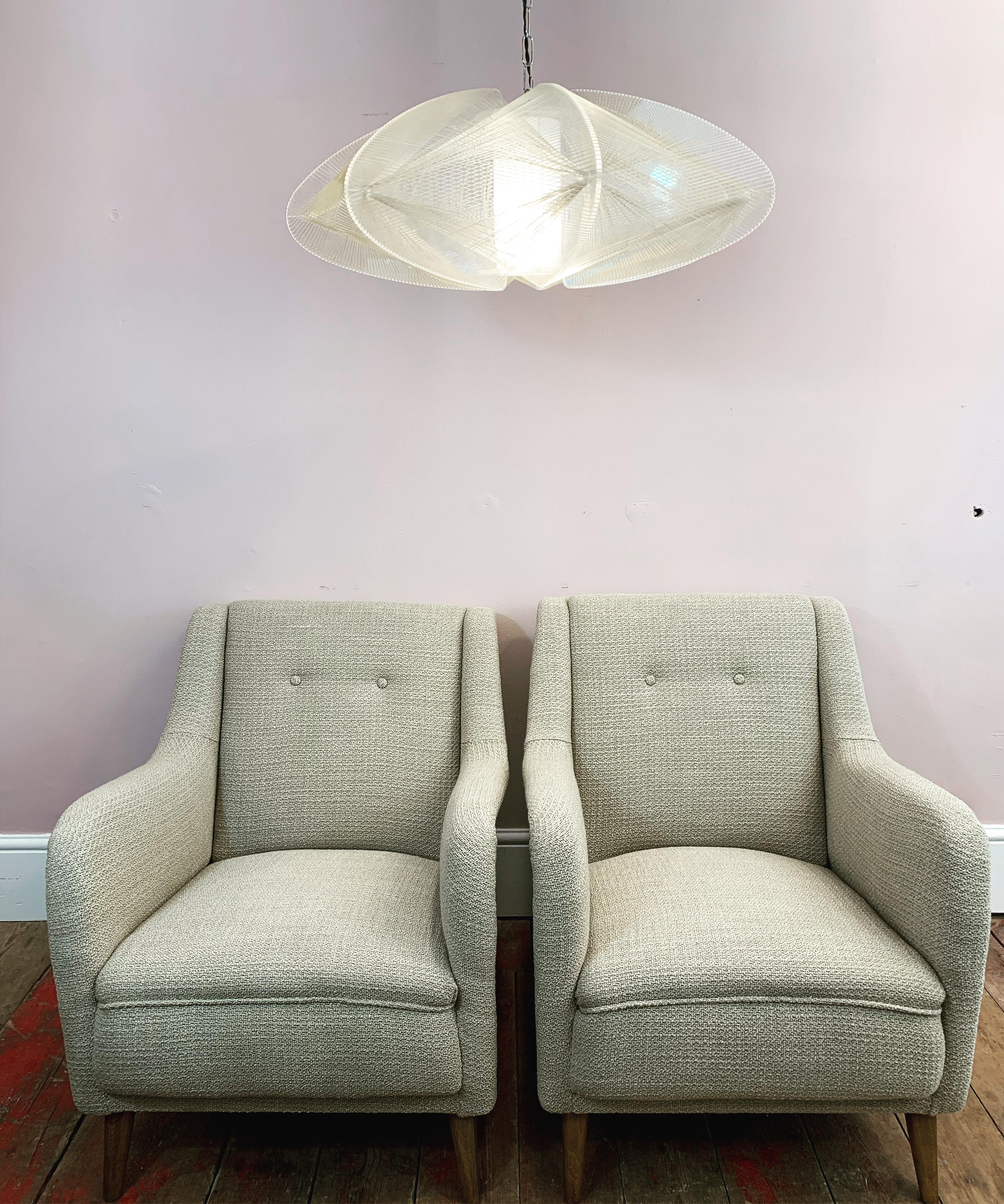 An incredibly comfortable pair of 1950s French armchairs with deep sprung seats reupholstered in Romo Group's Kirkby Design fabric's Loop Flax. The restored splayed legs have been stained and refinished with a matt varnish. Two feature buttons