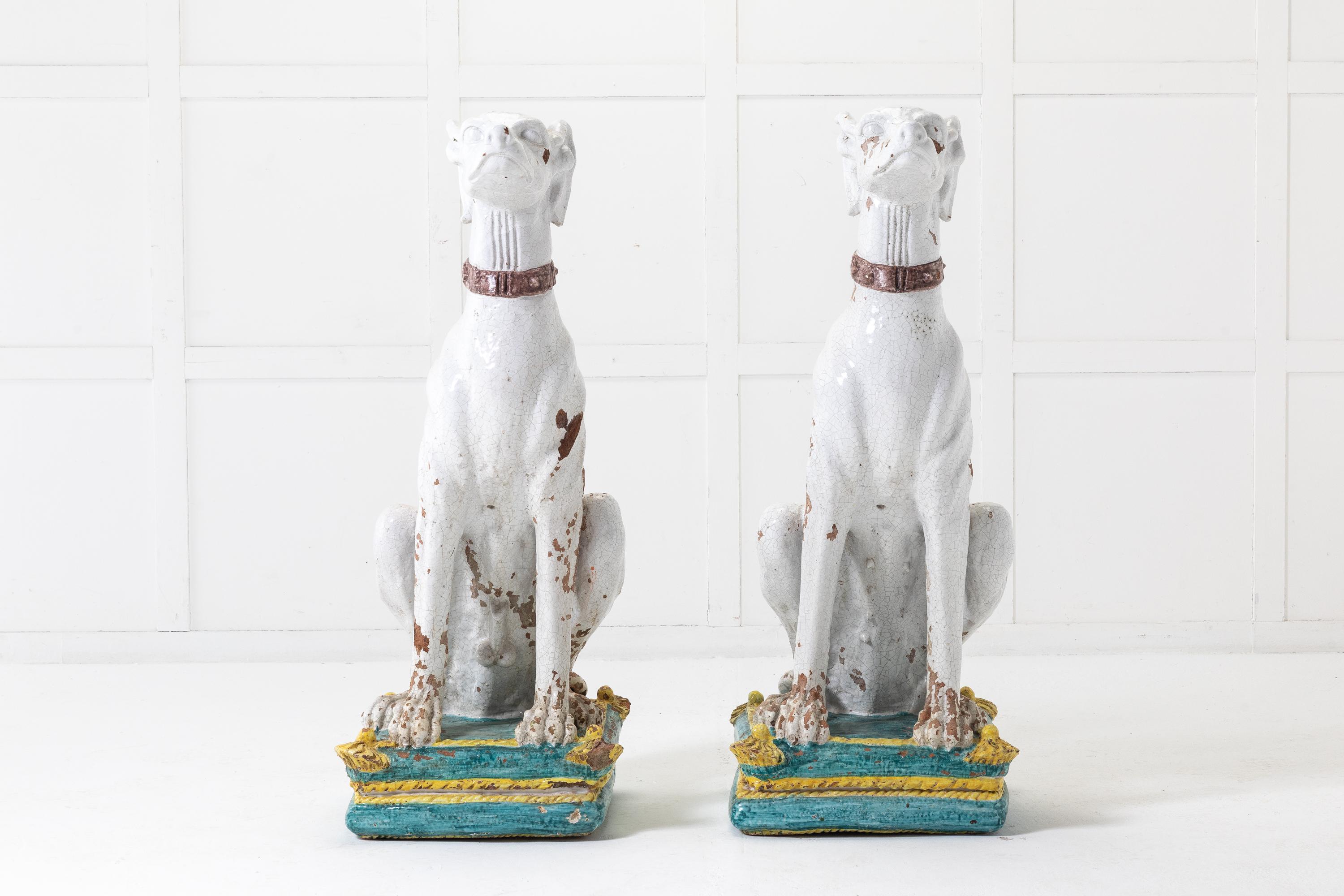 A fine and imposing pair of Italian 1950s majolica glazed dogs, male and female. Each one fitted with a wide collar, realistically modelled with expressive faces and poise, elegantly seated on their bright coloured cushions.

Wonderful decorative