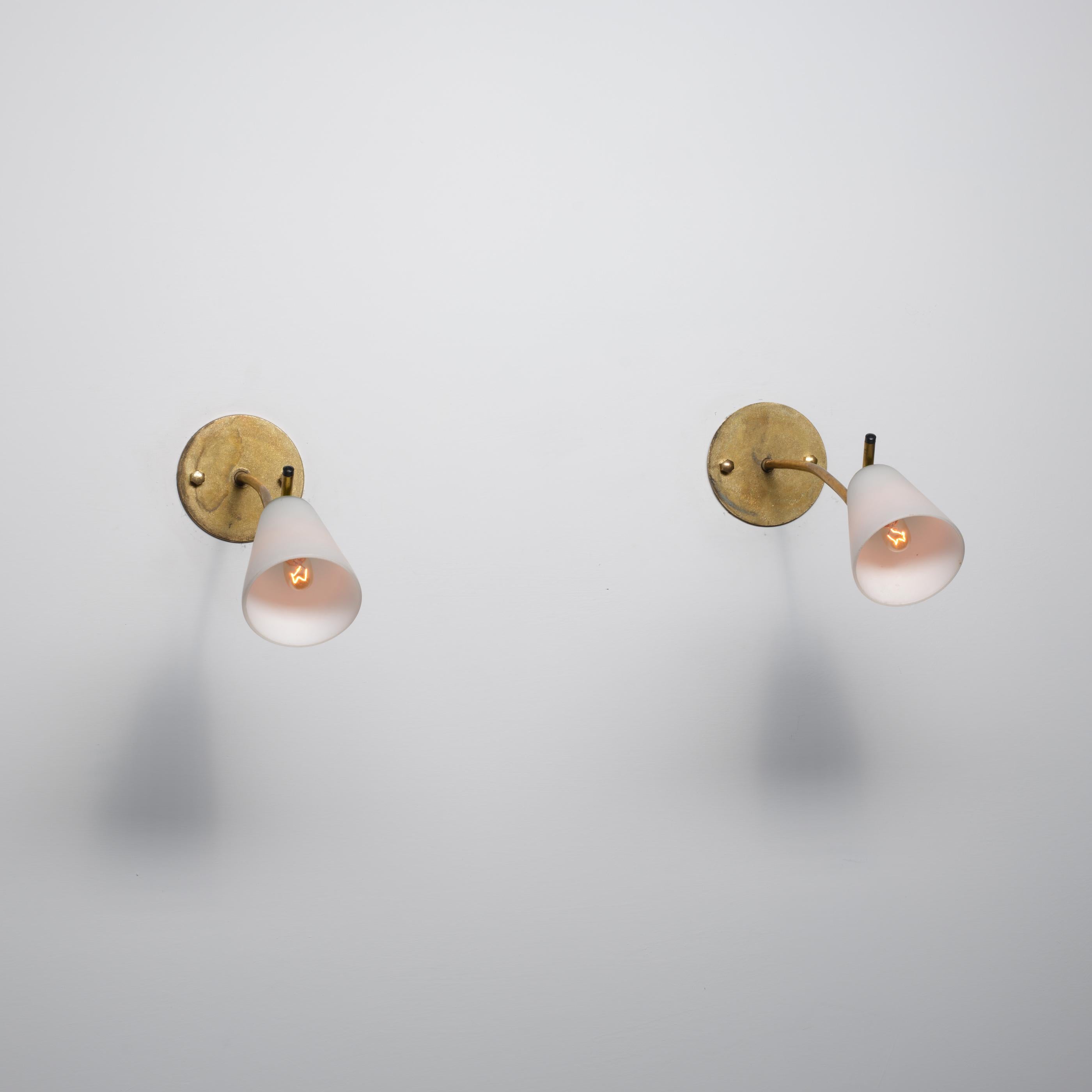 Pair of elegant Italian wall sconces from the 1950s, featuring gently curved brass arms and tapered opaline glass shades. The matt opaline diffuses a soft, warm light when illuminated and maintains a clean white appearance when switched off.

The
