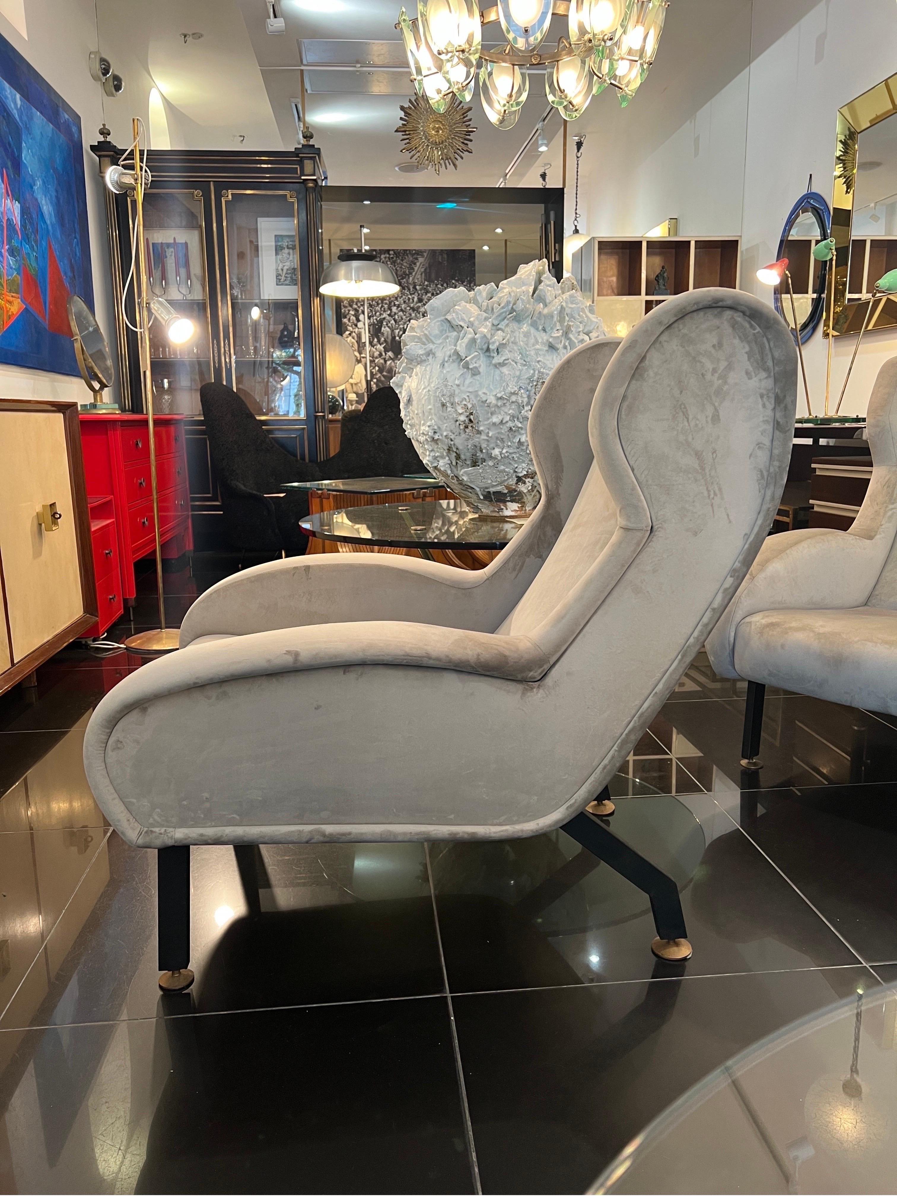 A stylish pair of 1950s armchairs slightly reclining to provide extra comfort. The pair have been newly upholstered in high quality grey stone colour velvet. The legs & the structure are made from black metal with brass discs.