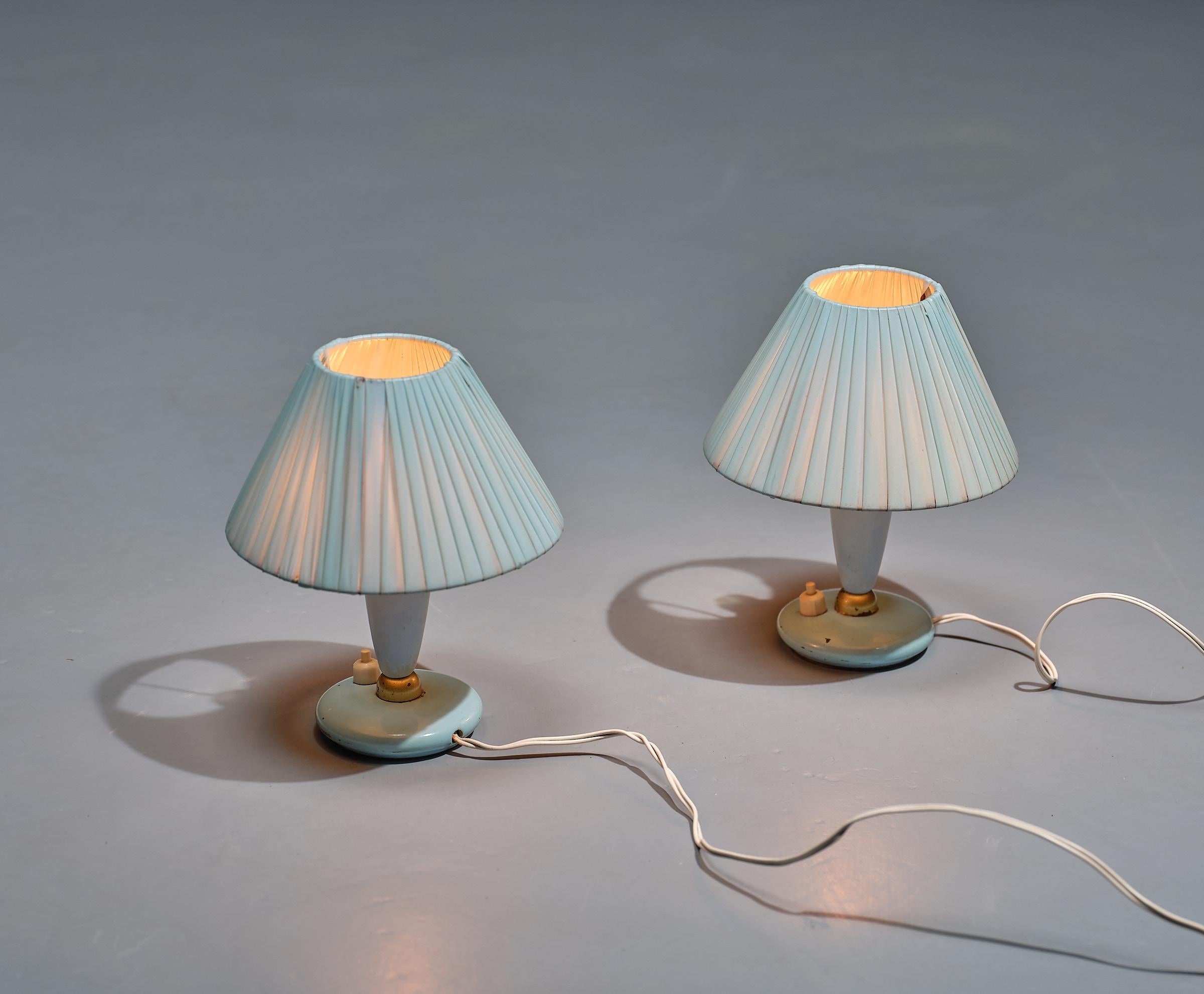 Presenting a pair of midcentury modern Italian bedside lamps from the 1950s, exuding timeless elegance and charm. These abat-jour lamps feature synthetic fabric lampshades, wooden bodies, and brass details, all in a soothing blue color that carries
