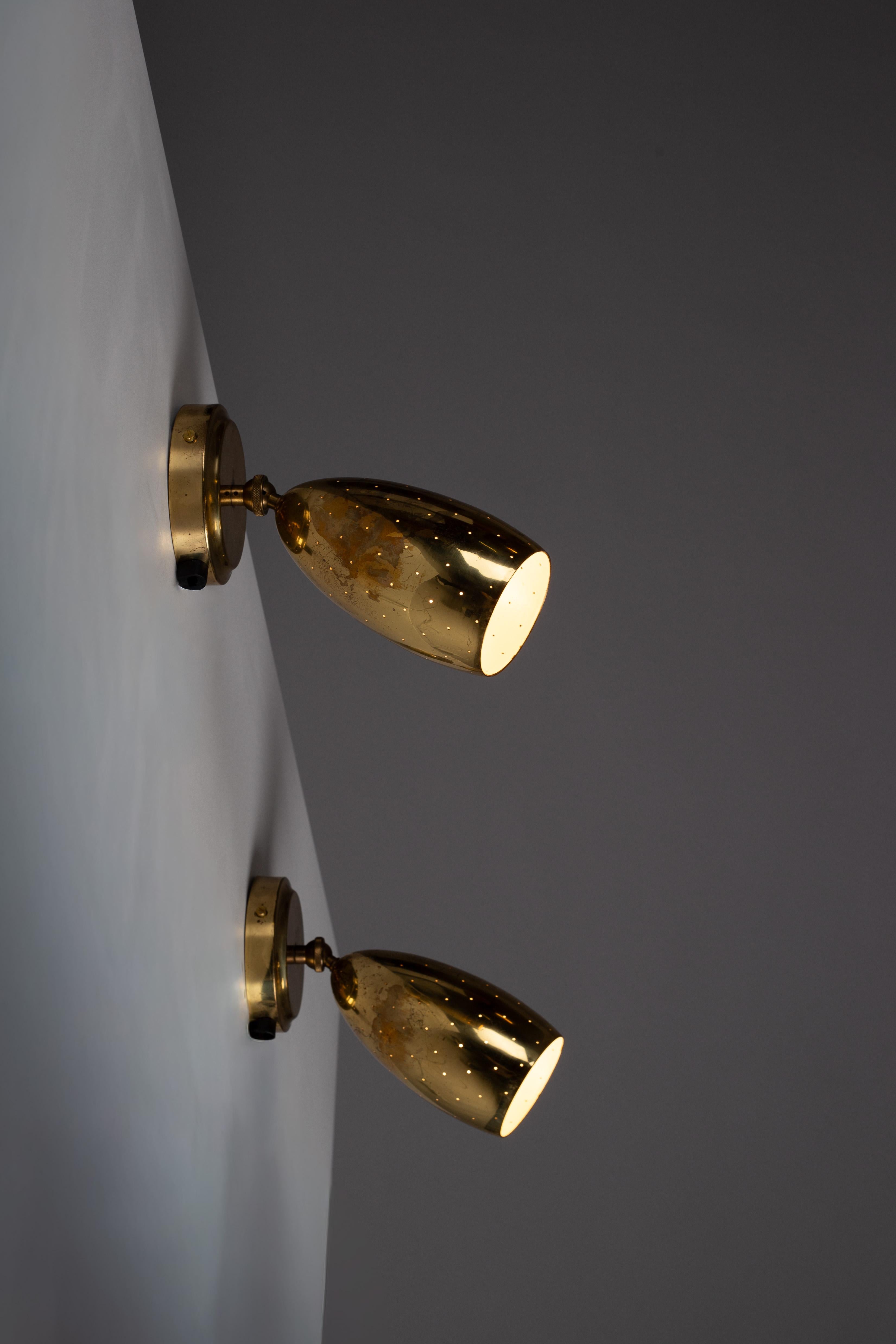 Eleva tu espacio con el par de apliques de pared Itsu EY 67 de latón perforado de los años 50, procedentes de Finlandia. Estas exquisitas piezas, ajustables gracias a la rótula, se adaptan perfectamente a tus necesidades de iluminación. Las