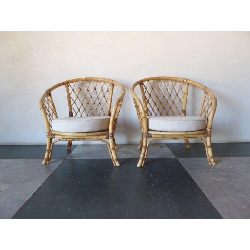 Pair of 1950s Rattan armchairs with Linen seats with criss-cross woven pattern rattan at back. Circular back / arm shape, these chairs exude mid-century modern lines and character. Perfect addition to any room. 
 
