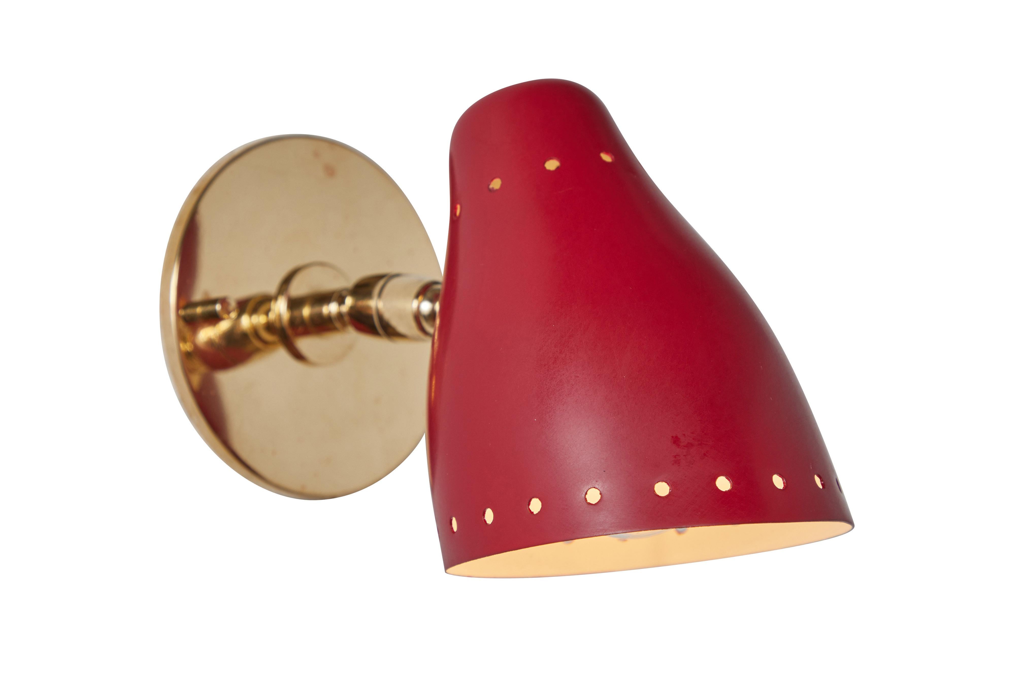 Pair of 1950s red perforated sconces attributed to Jacques Biny. A exceptionally clean and simple design executed in brass with red painted perforated metal shade. Lamps rotate freely on adjustable swivel. Quintessentially midcentury French in its