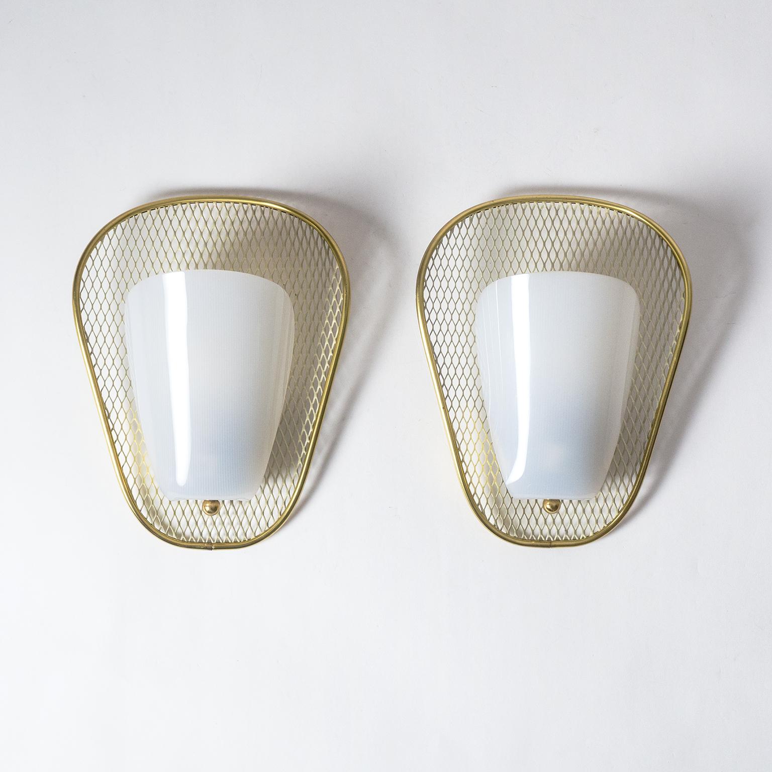 Classic midcentury sconces in the style of Jacques Biny. An organic shaped and curved backplate made of an expanded metal mesh, lacquered in ivory, with a brass rim. The diffuser is opaque acrylic with a ribbed surface on the inside. Very good