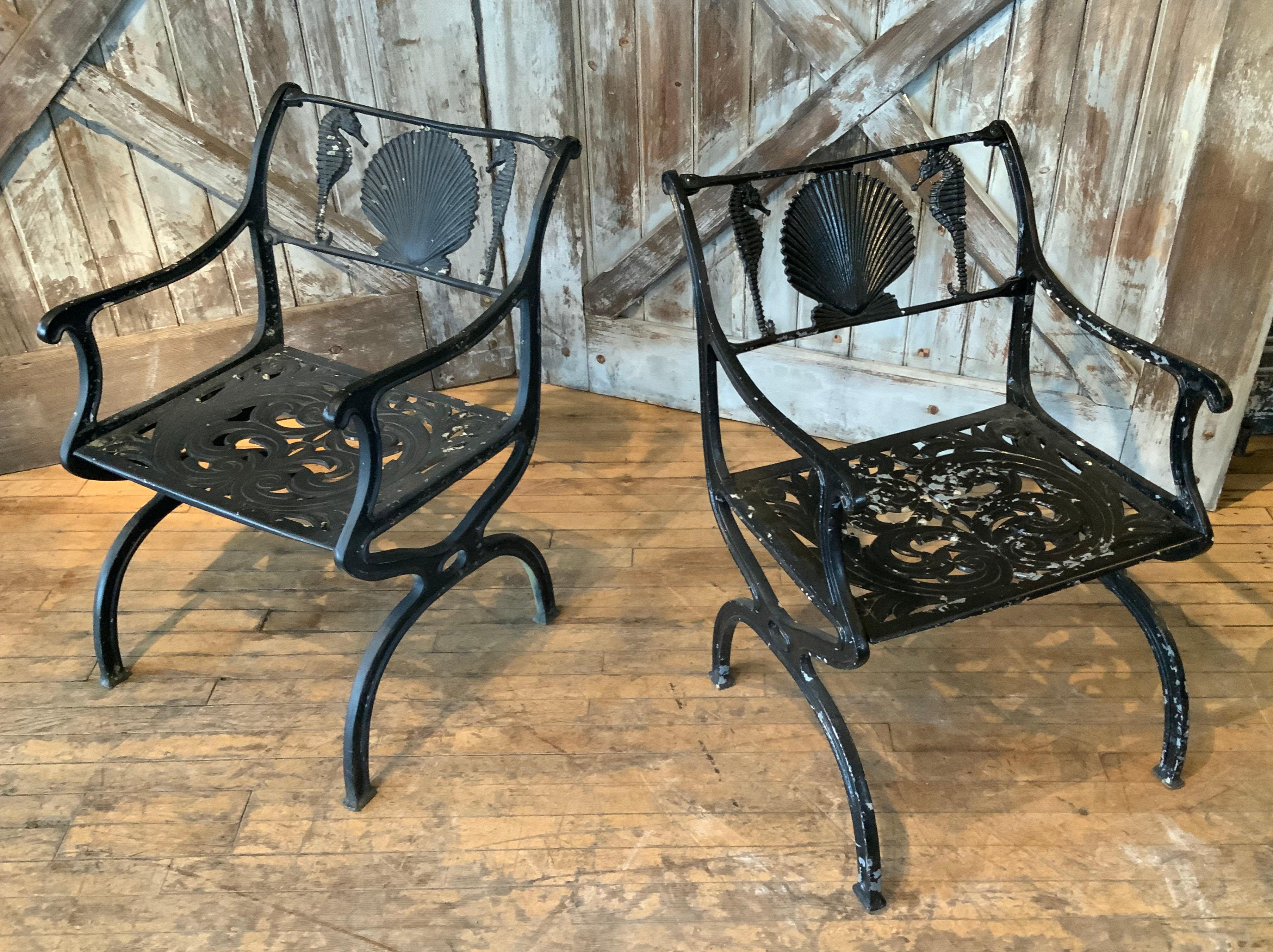 a classic pair of 1950's cast aluminum garden chairs with Seashell and seahorse motif in the seatback. beautiful scale and design. the orignla black finish is worn somewhat as pictured. made by Molla in the 1950's, a large group of these chairs were