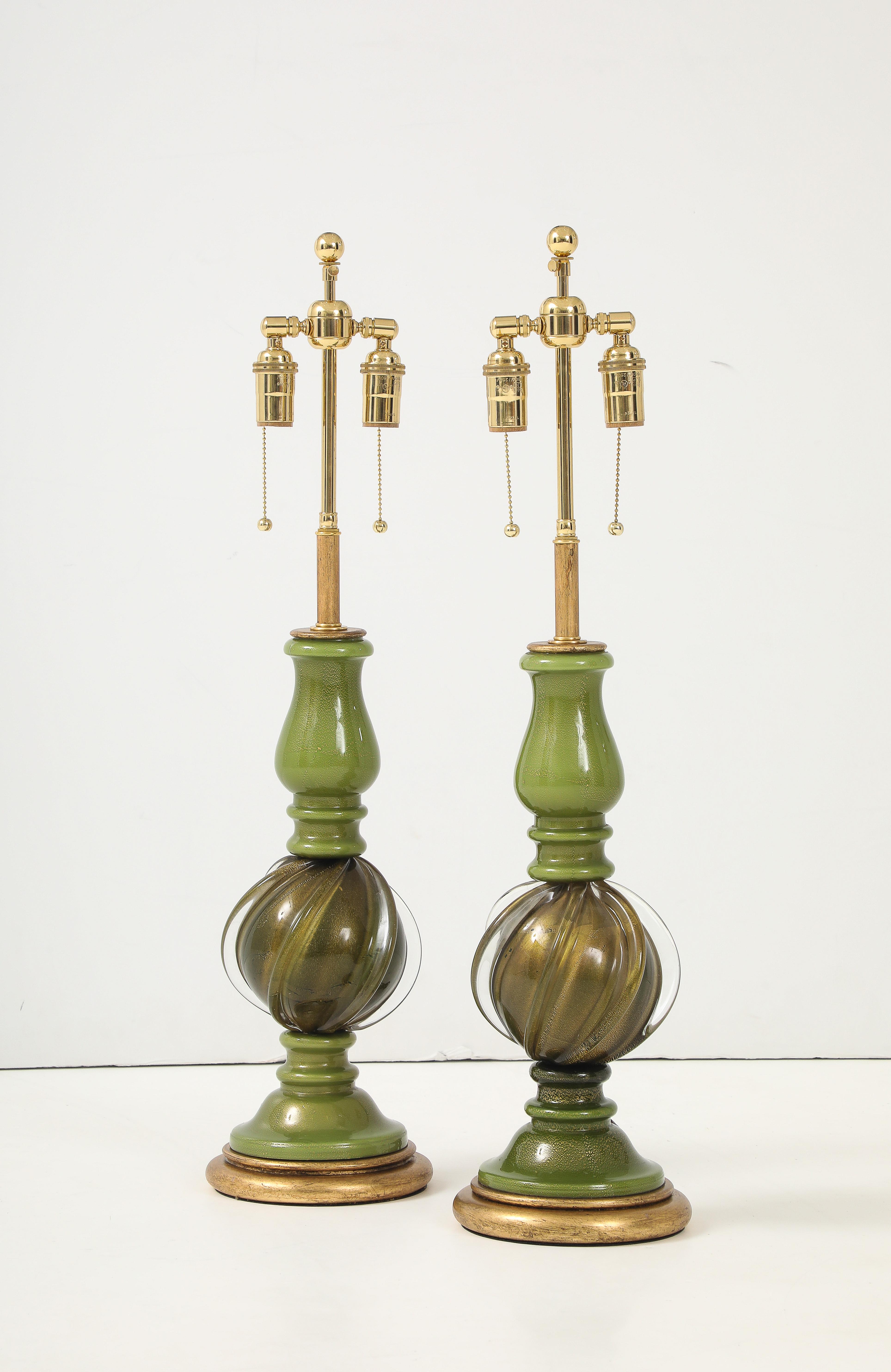 Bellissima coppia di lampade in vetro di Murano verde con piccole inclusioni d'oro.
I corpi delle lampade in vetro poggiano su basi dorate e sono stati ricablati di recente con un cavo regolabile.
doppi cluster in ottone lucido e cordoncini in rayon