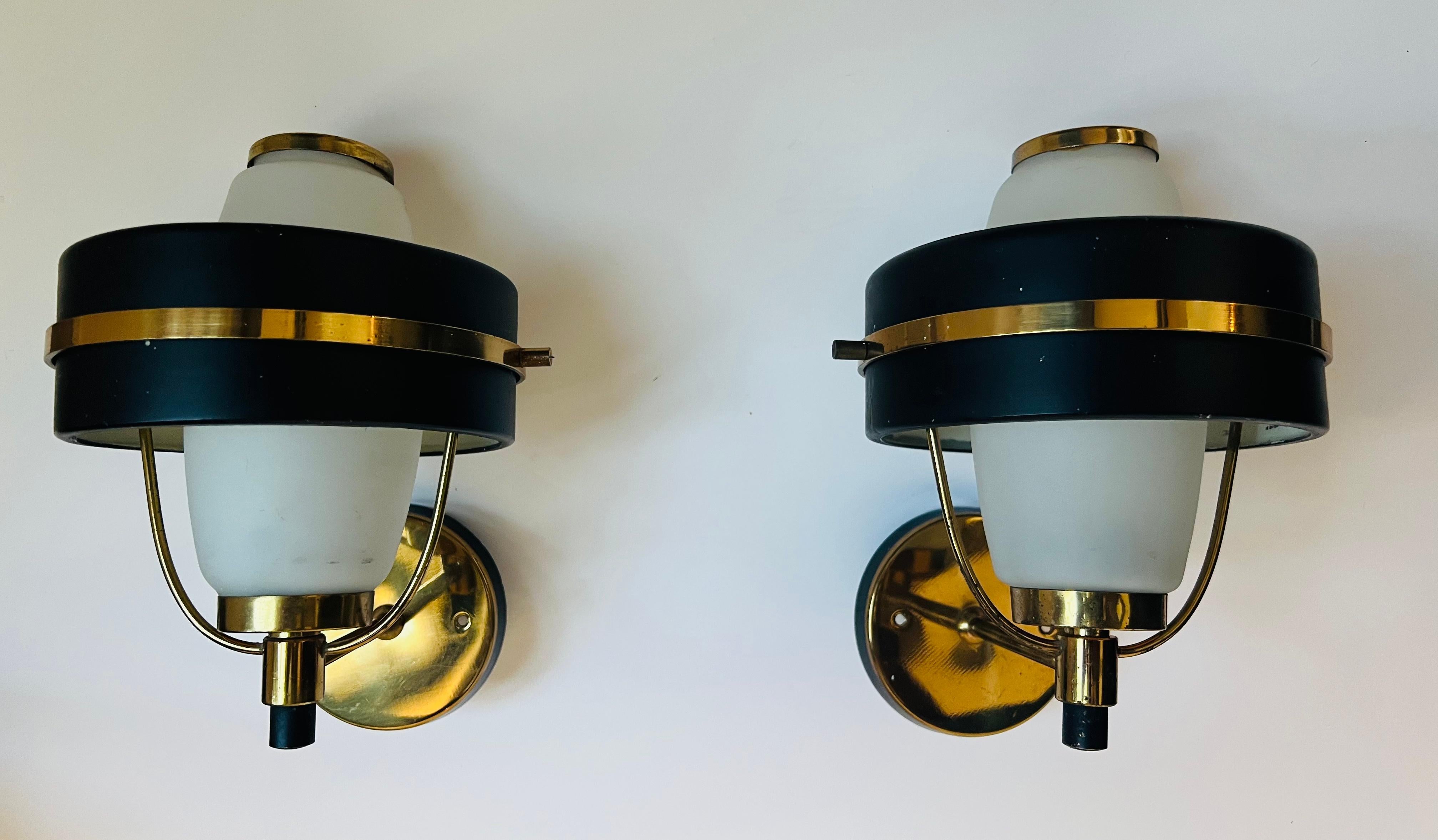 An original pair of 1950s Italian mid century sconces in golden polished brass and black enamel with white frosted glass shades. Rewired. One 120 watt candelabra socket each. Made by Stilnovo.
