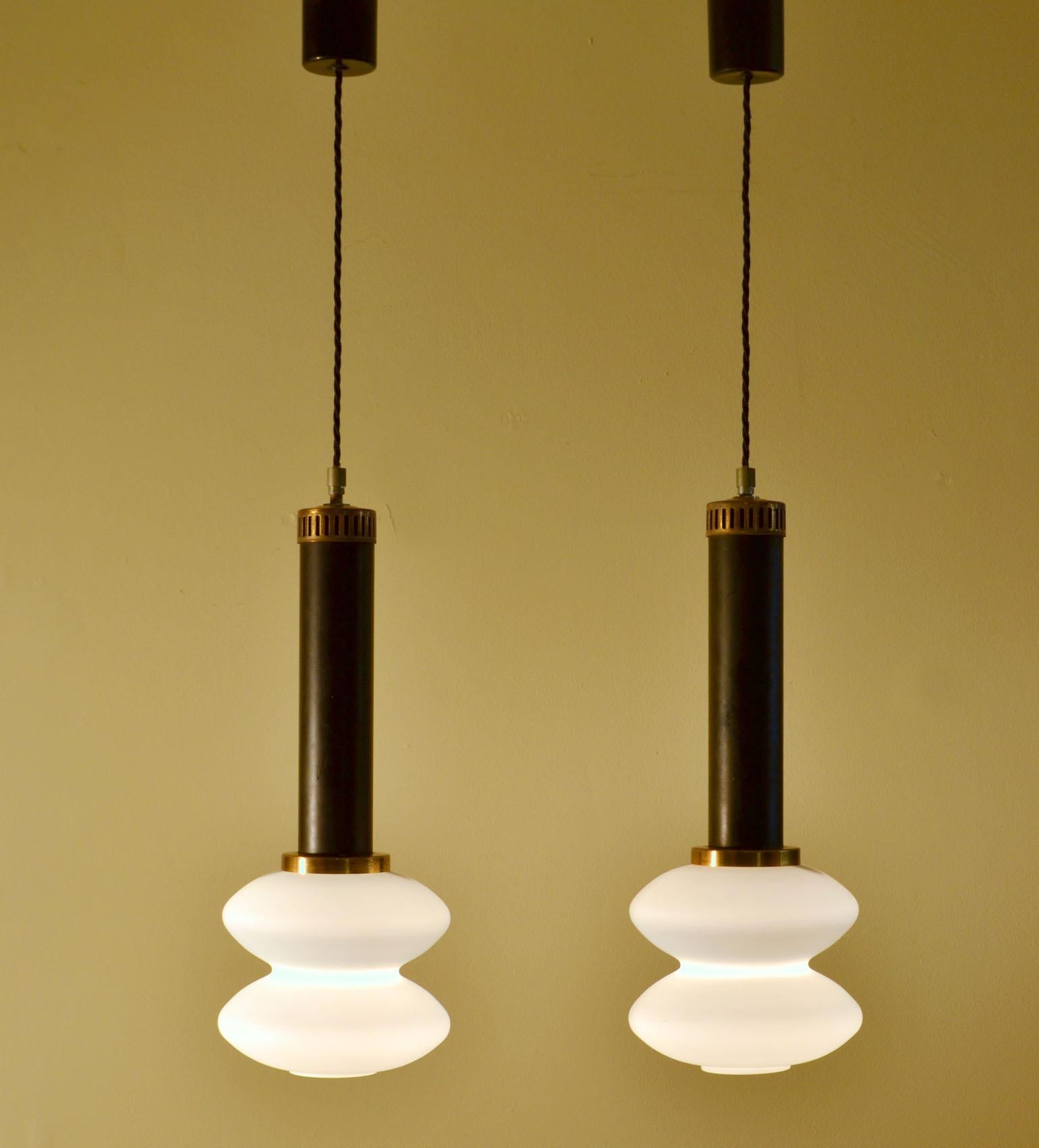 Pair of hand blown opaline diffuser shade pendant lamps on black and brass stem by Stilnovo 1950s.
Modernist shaped pendant lamps with curvaceous conical shaped milk glass hand blown shades. The lamps give very nice diffused warm light when lit and