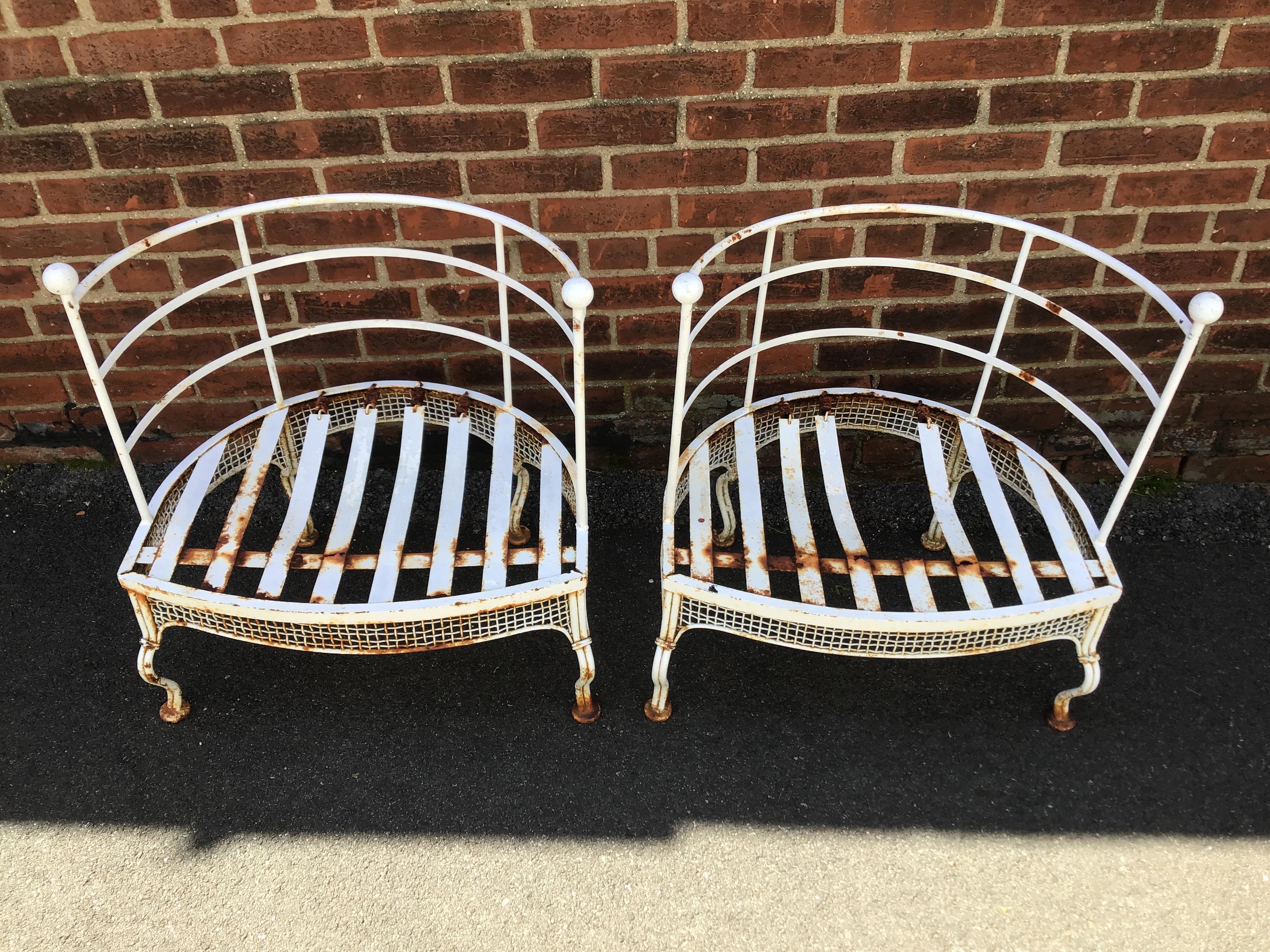 Pair of 1950s Woodard garden tub chairs. Chairs need painting. One metal strip on seating is gone.