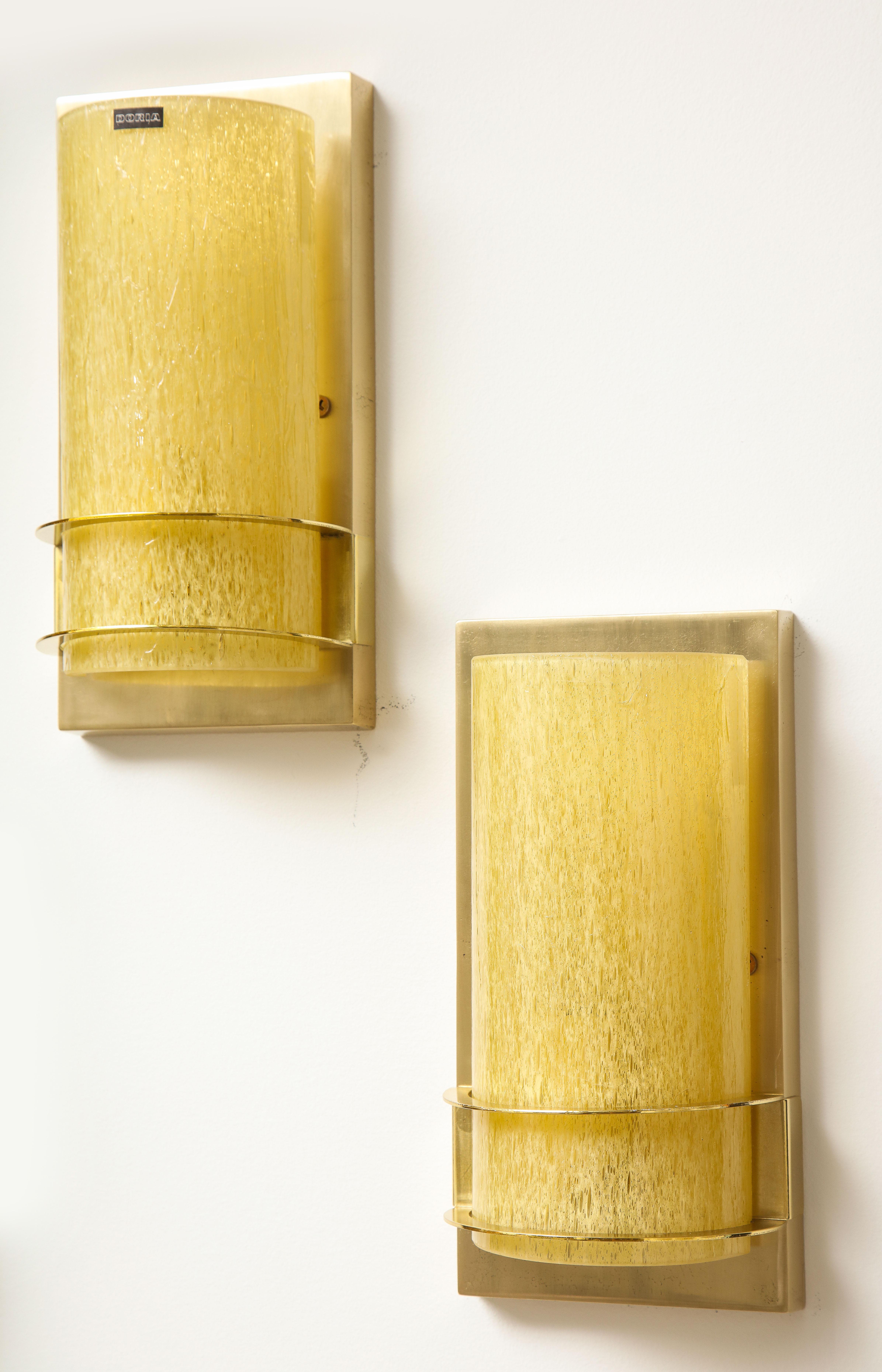 Pair of Amber glass sconces by Doria.
The half rounded textured glass sits in the polished brass rings.
The fixture is illuminated by a single light source which has been newly rewired for the US with a candelabra light bulb with a 40 Watt Maximum.