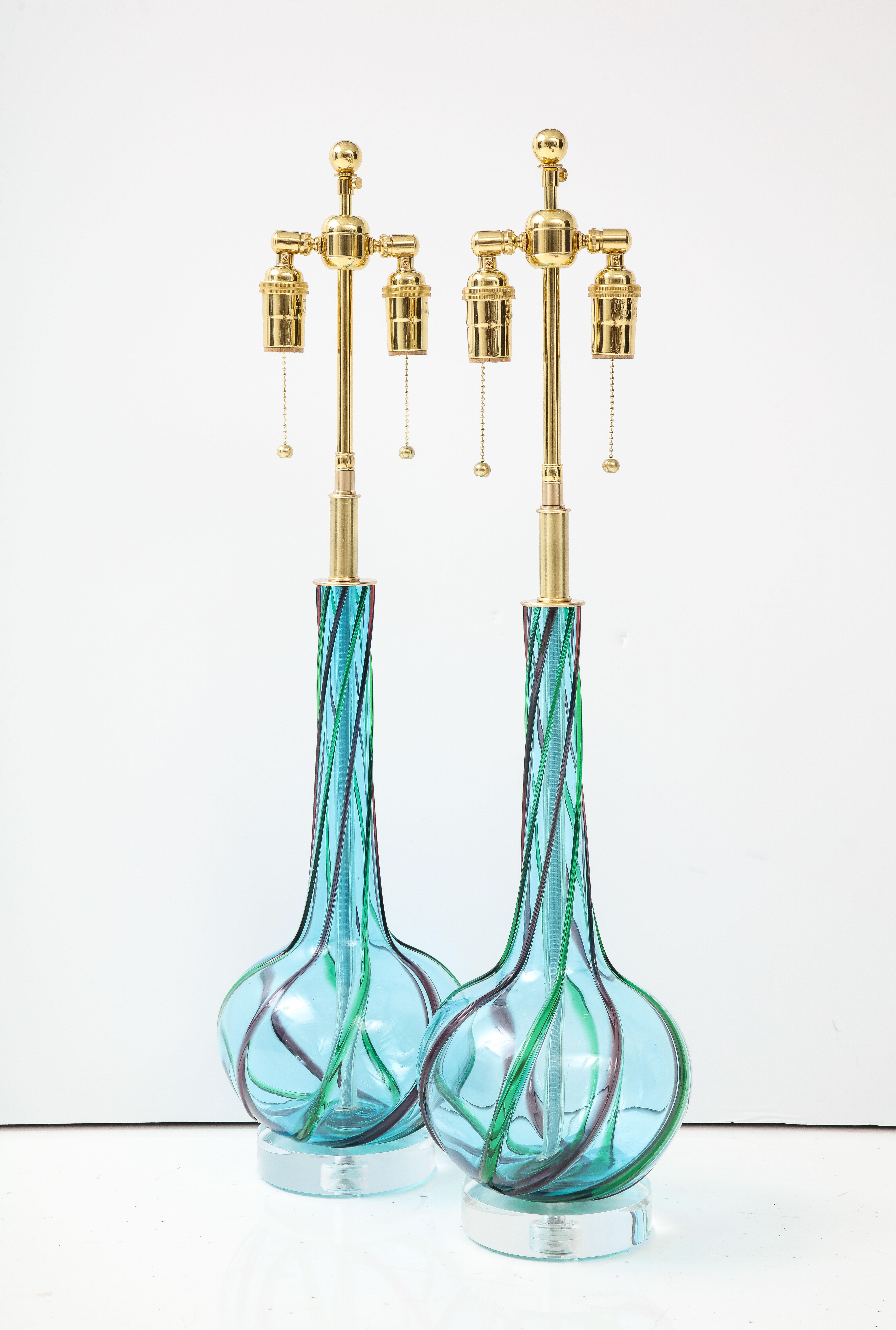 Pair of 1960's Blue Murano glass lamps with Green and Amethyst Ribbons.
The lamps are mounted on thick lucite bases and have been Newly rewired with adjustable polished brass double clusters that take standard Light bulbs.