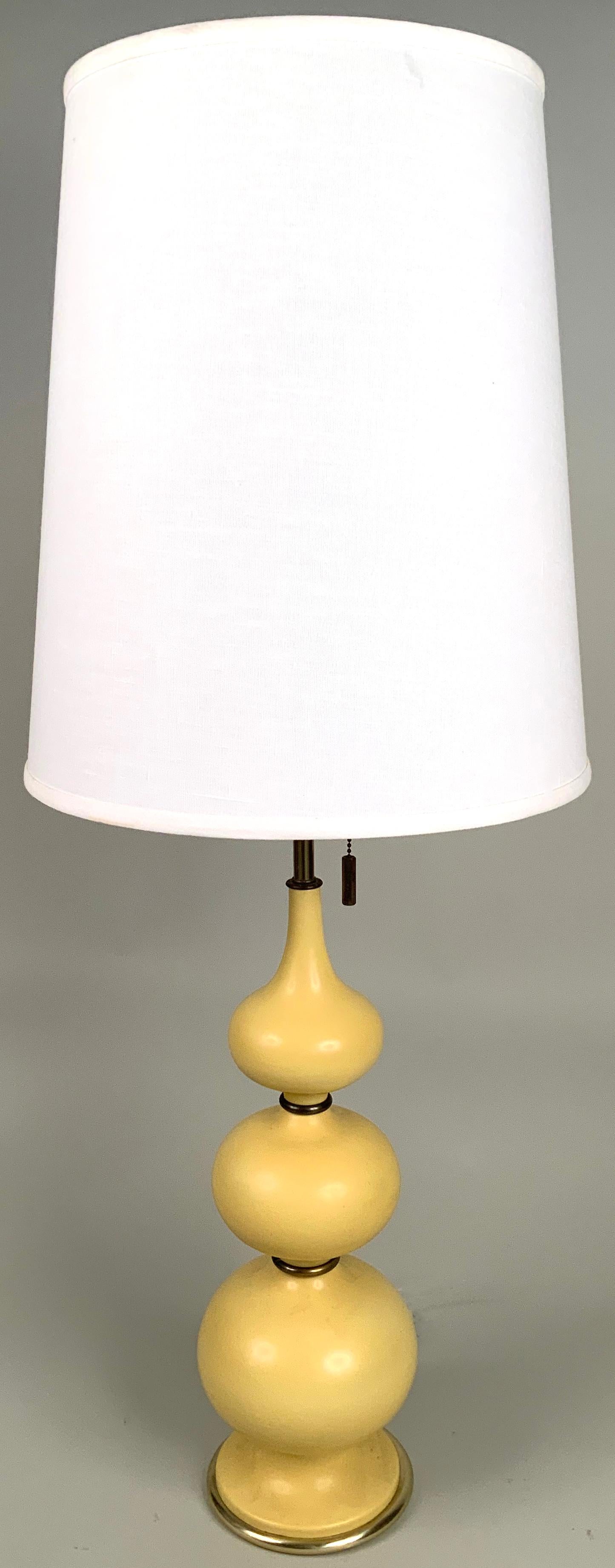 A beautiful pair of vintage 1960s table lamps designed by Gerald Thurston for Lightolier. the bases with a series of graduated ceramic orb shaped, separated by brass rings, in a pale butter yellow. both with Ligholier's signature three socket