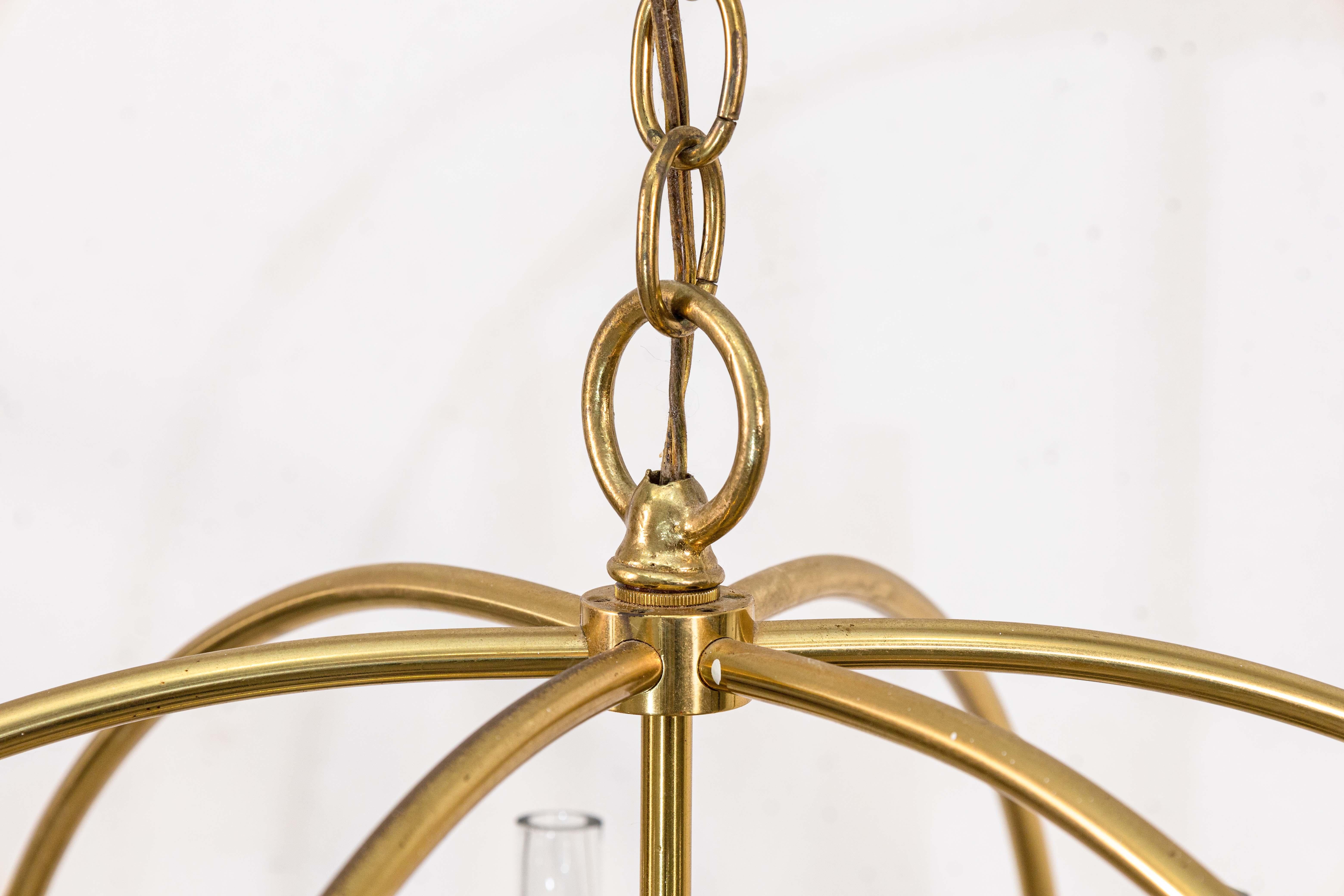 A pair of 1960s Feldman brass chandeliers. These incredible vintage chandeliers feature a polished brass frame, with glass and smoked lucite accent details. The chandelier hangs from the polished ceiling housing via a wired chain of the same brass.