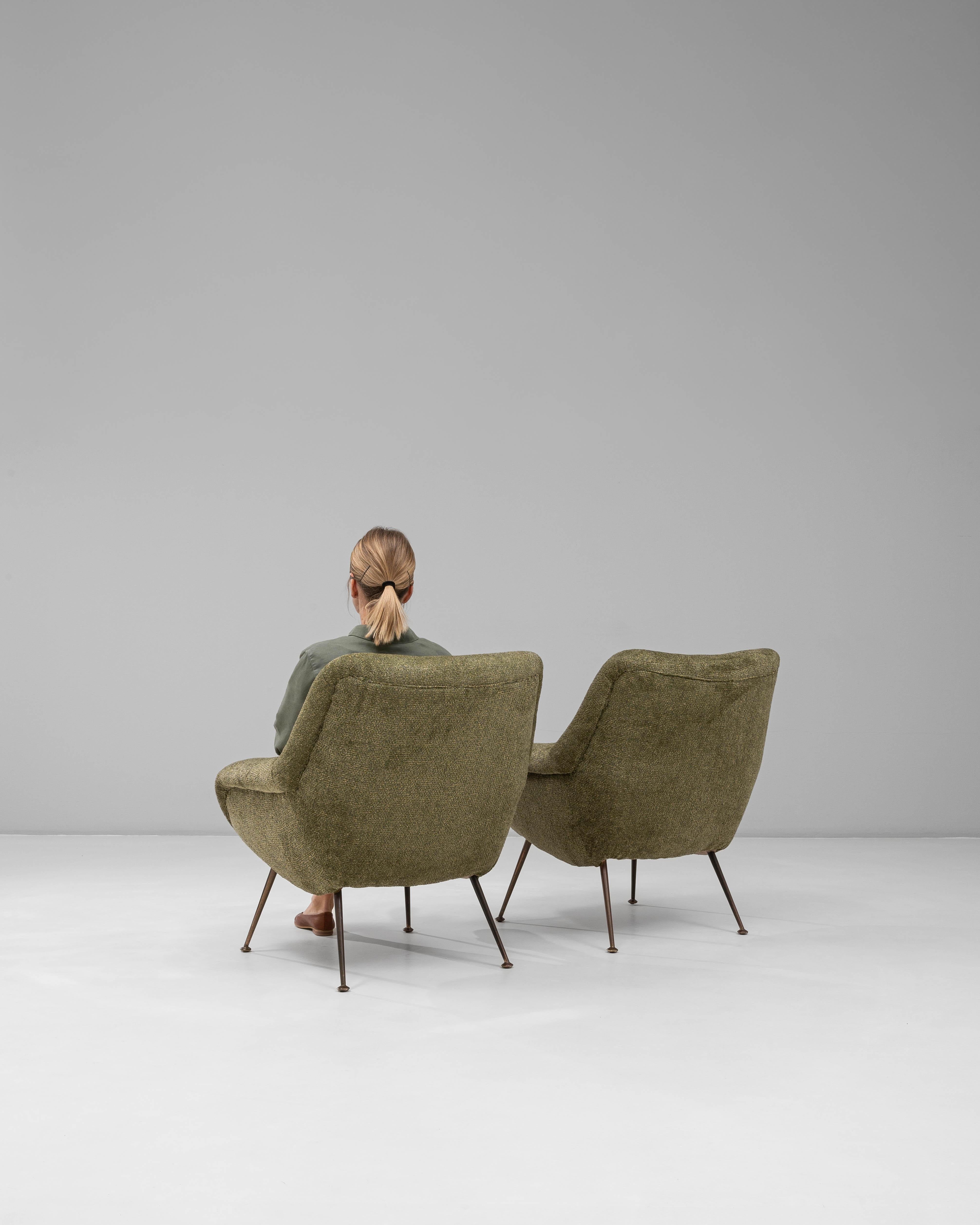 This pair of 1960s French green Art Deco upholstered armchairs features a sculptural silhouette that blends mid-century comfort with subtle Deco influence. The gently curved backs, rounded arms, and plush seat cushions create an inviting, organic