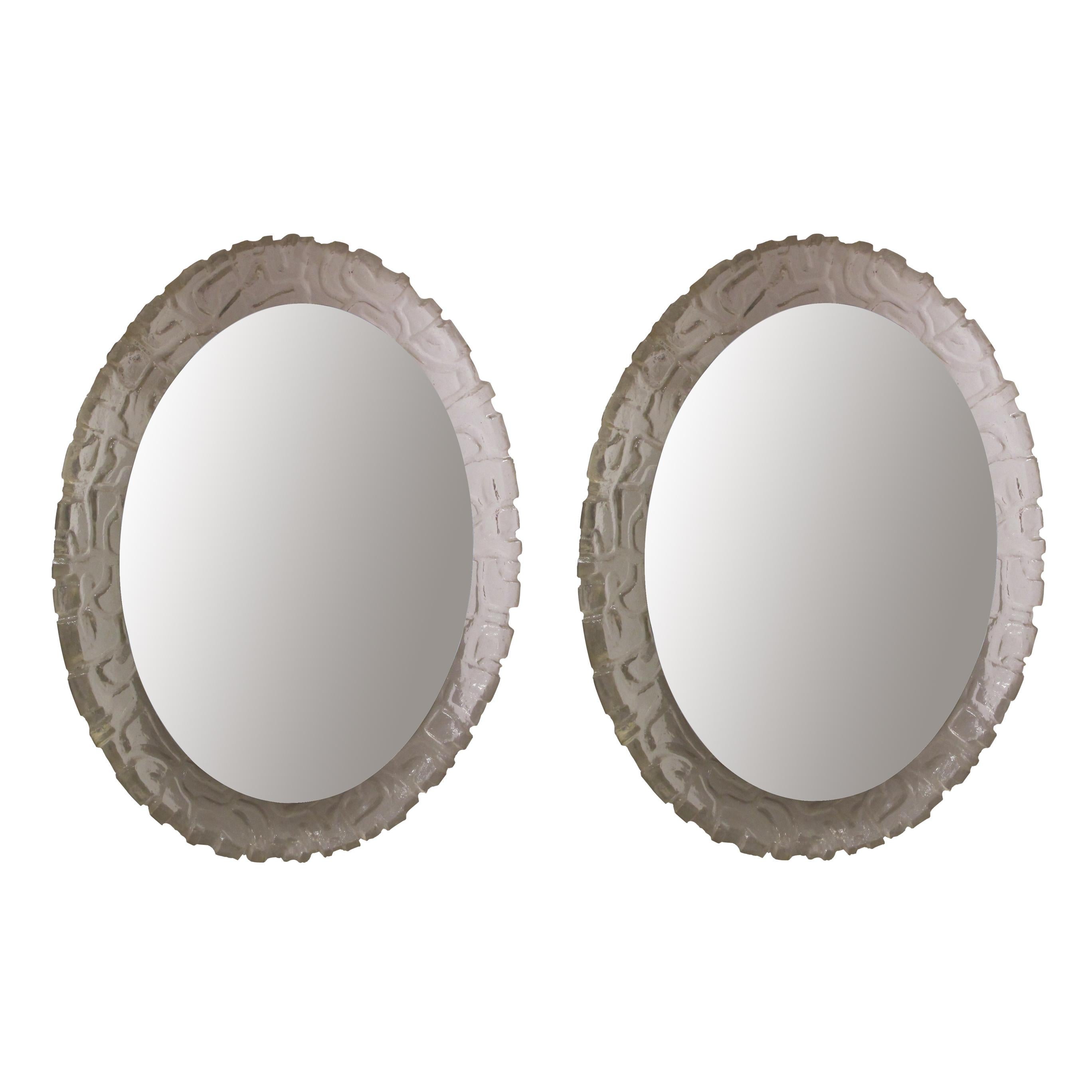Pair of oval backlit wall mirrors with a moulded Lucite frame. Manufactured by Balschbach in Germany in the 1960s. The light reflects through the textured Lucite frame which gives a warm, ambient, glowing light evenly throughout the whole frame. The