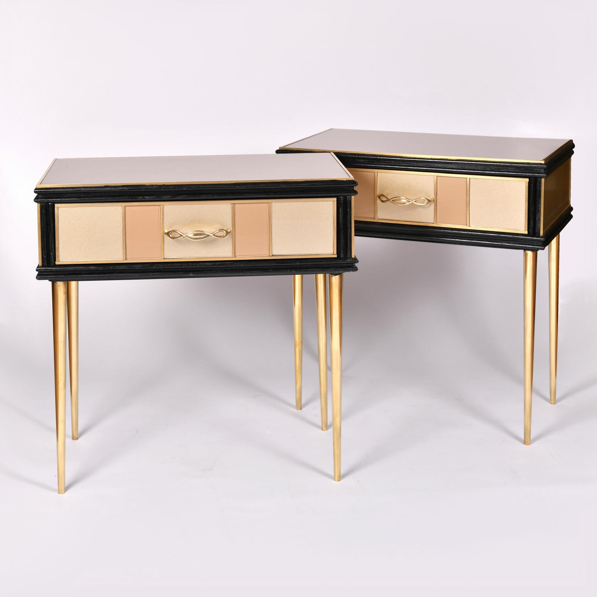 Elegant side tables, each with a single drawer, paneled in alternating gold and cream glass with brass trim and brass twisted handles. 

Tapered brass legs.

Measures: 60 cm high x 57 cm wide x 31 cm deep (34cm including handle).