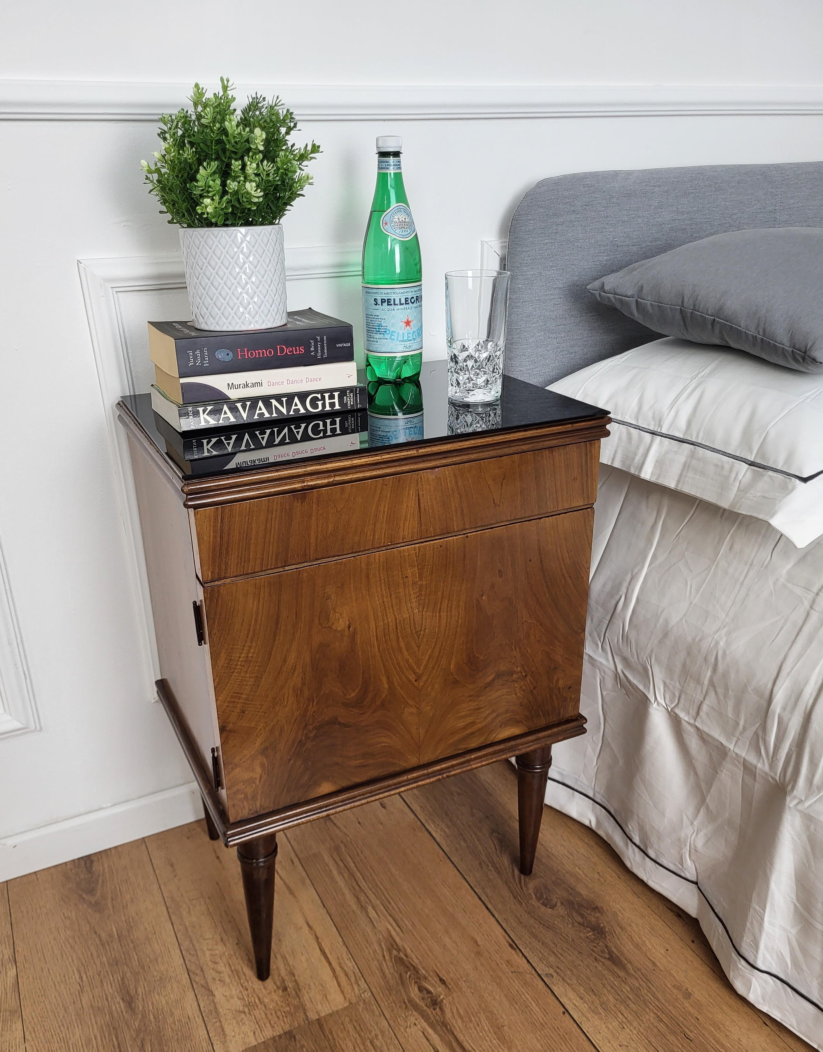 Very elegant and refined Italian 1960s Mid-Century Modern design and geometrical shape, pair of bedside tables in walnut wood, central drawer and front door completed by black glass top. Those nightstands make a great look in any style bedroom, as a