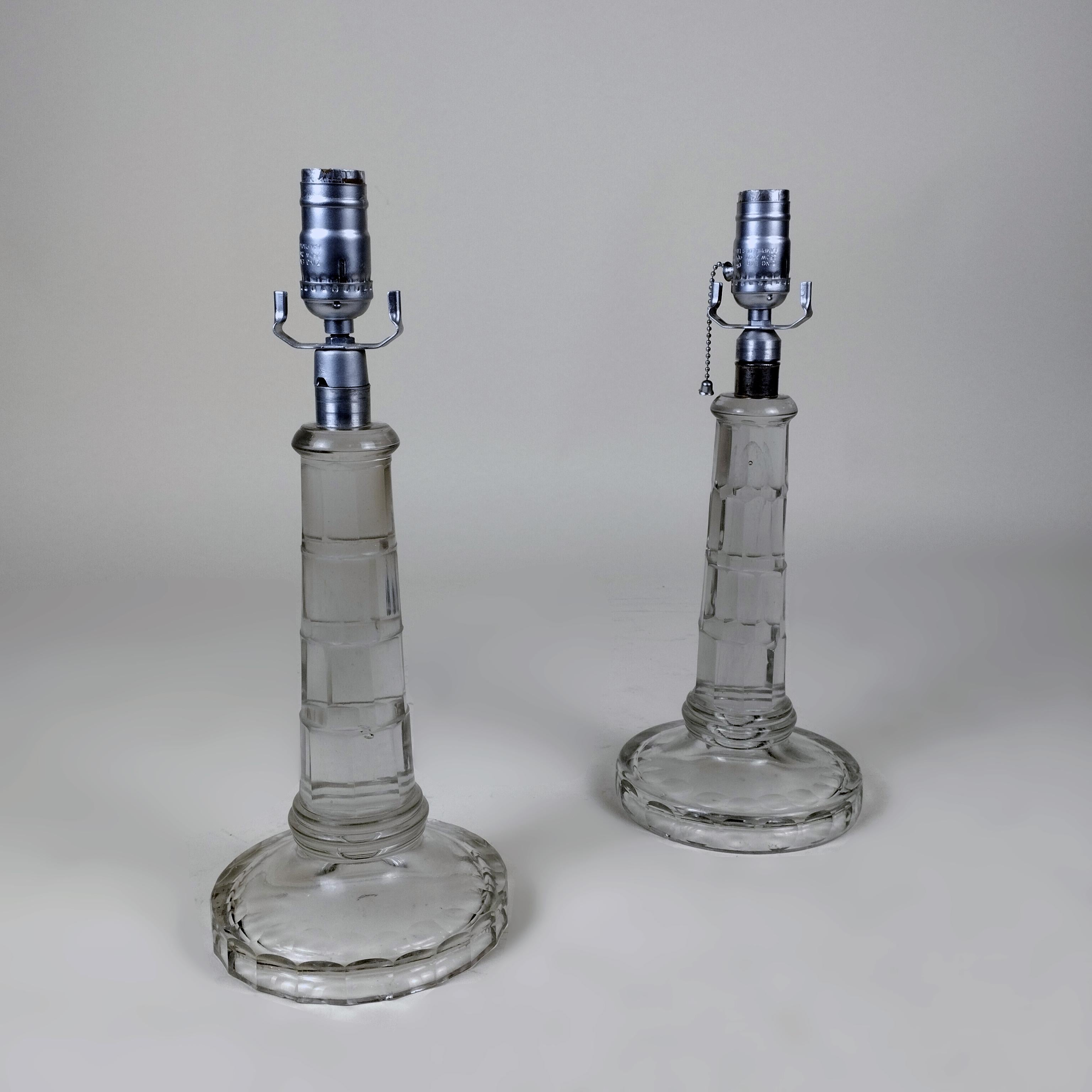A 1960's pair of cut glass table lamps. The glass body shows facet cut design. Sockets and shade holders are made of silvery metal. No shades included.