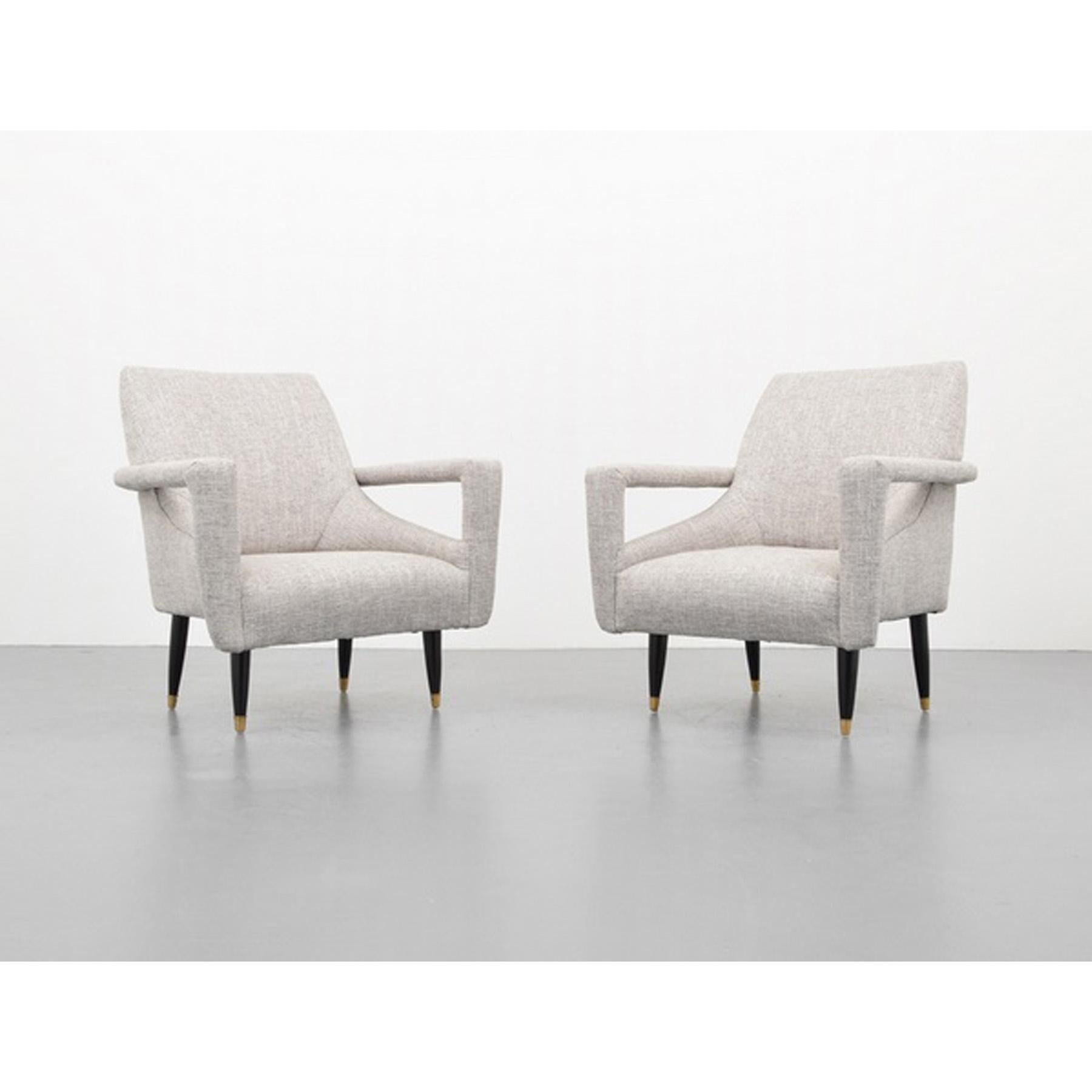 A pair of Mid-Century Modern lounge chairs in the manner of Italian designer Ico Parisi. Upholstered in a light gray fabric, with black wooden leg that feature brass detailing, Circa 1960's.