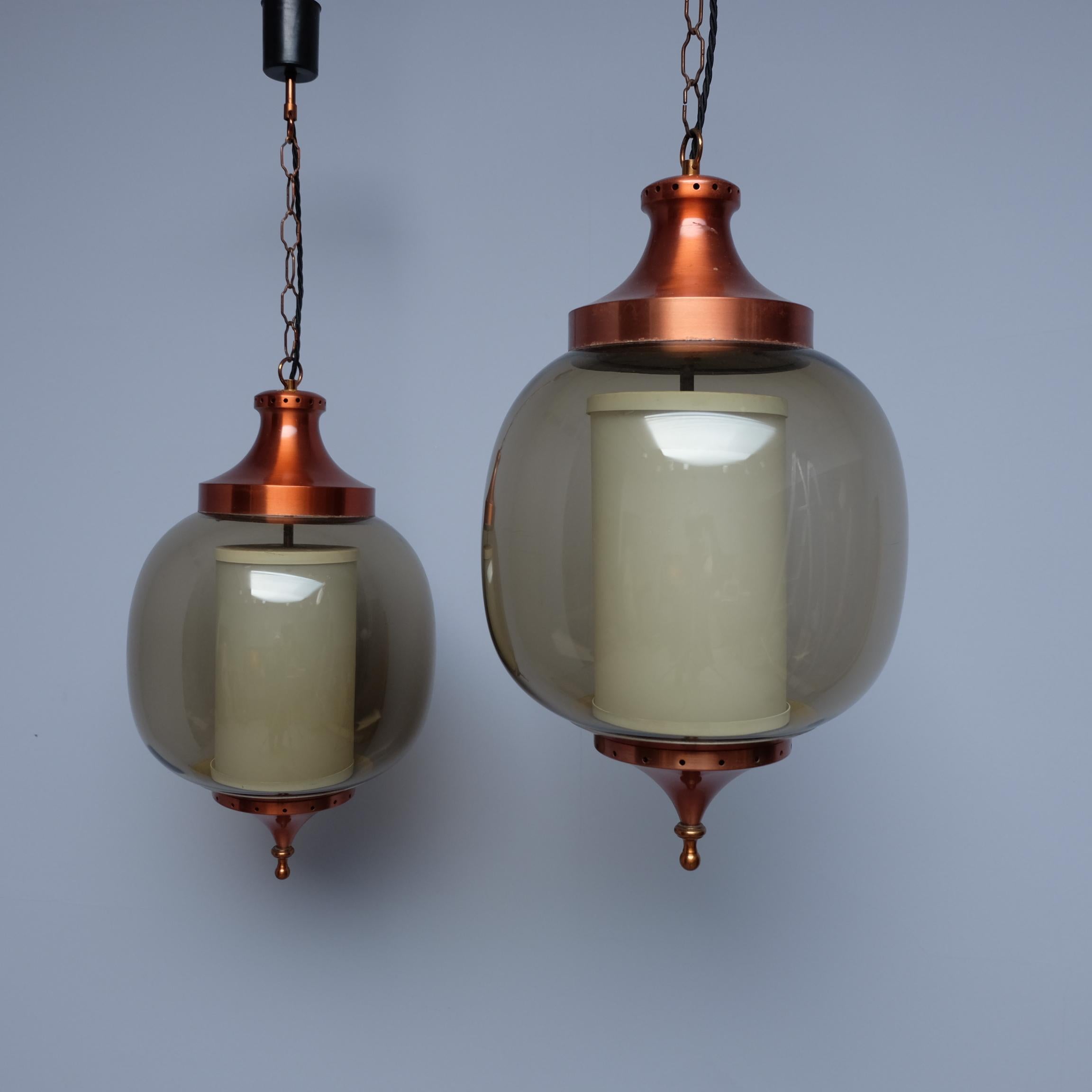 A stunning pair of 1960s French 'Lumiere' pendant lights formed in the shape of lanterns. Made from anodised, copper-coloured, aluminium, with smoked glass bulbous shades. The white tubular glass inner shades shed a warm glowing light giving the