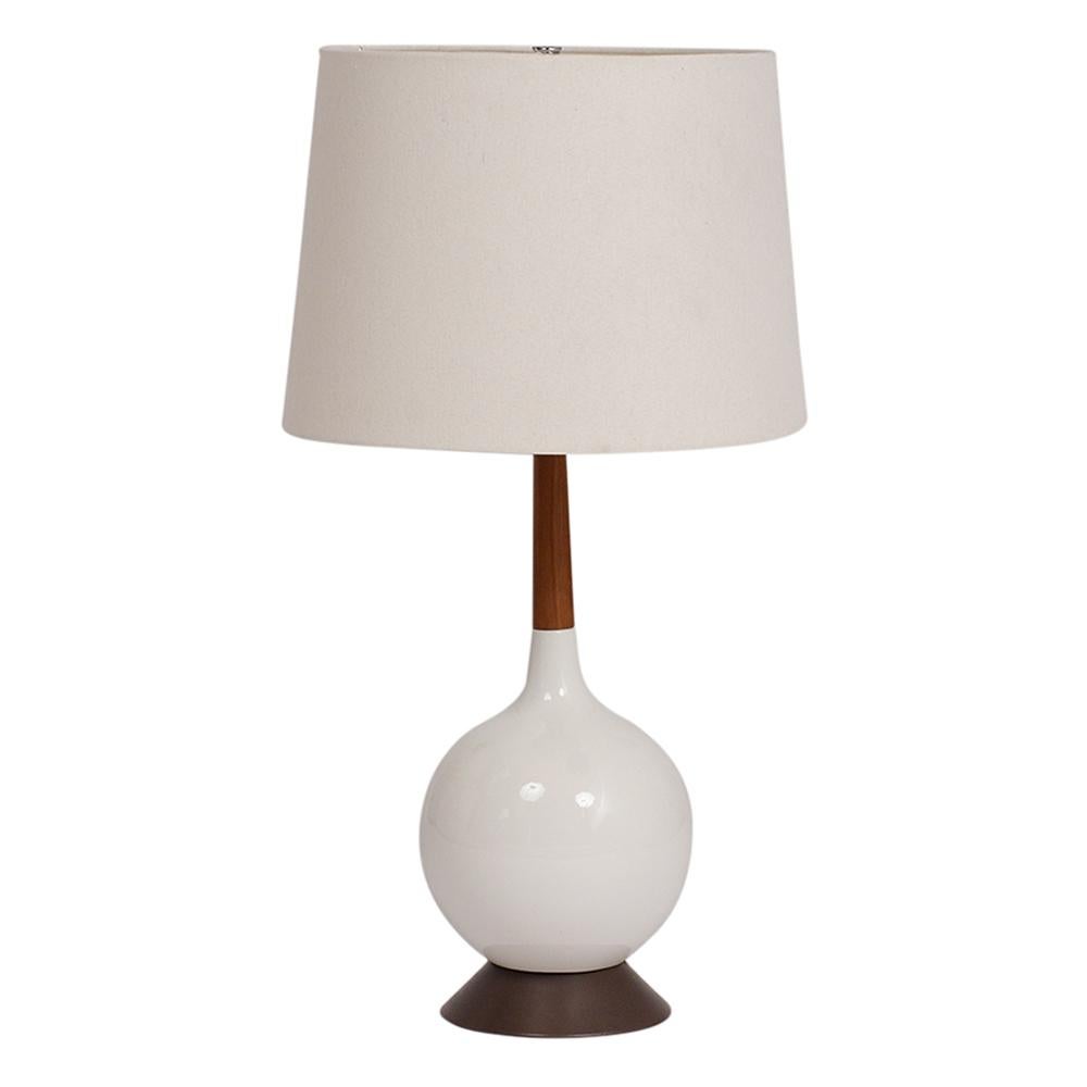 This pair of Mid-Century Modern table lamps features a circular ceramic body with a white glaze and a natural patina. The circular base is made of bronze metal, and the walnut wood neck has a patinated finish. It also has a brand new off white linen